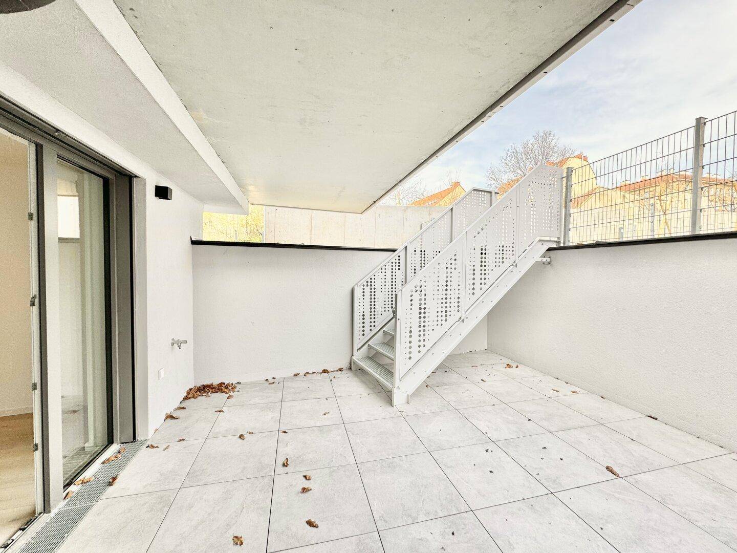 Große geflieste Terrasse mit Treppenzugang und Blick auf umliegende Gebäude.