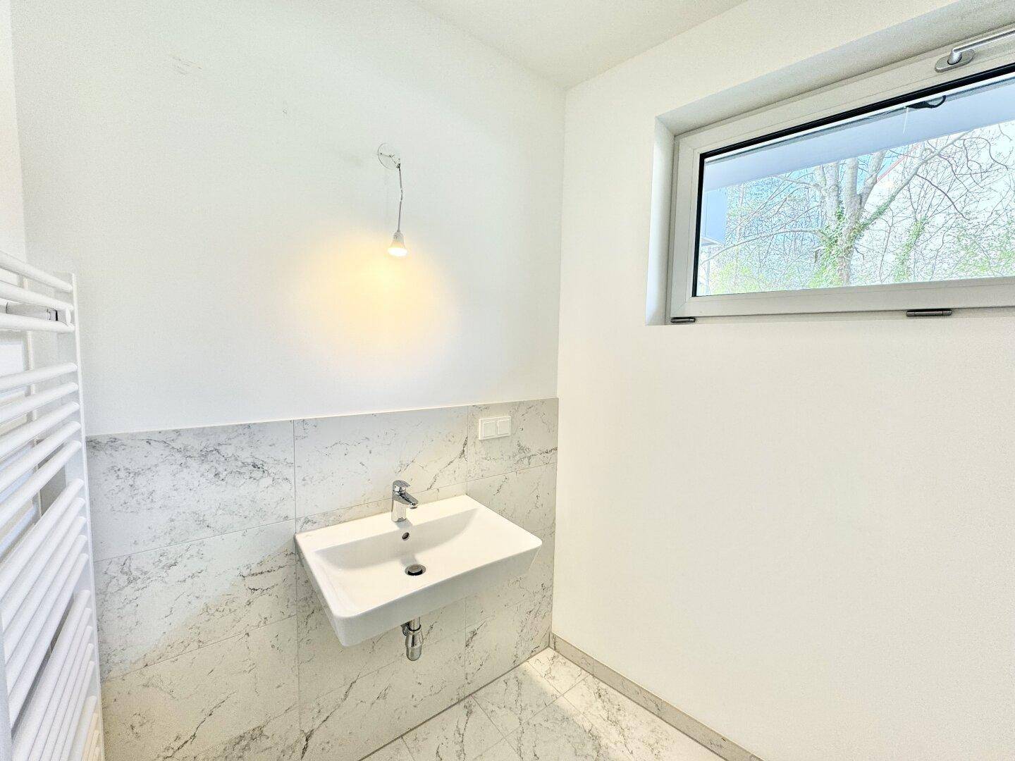Modernes Badezimmer mit Waschbecken, Marmorfliesen und Fenster für Tageslicht.