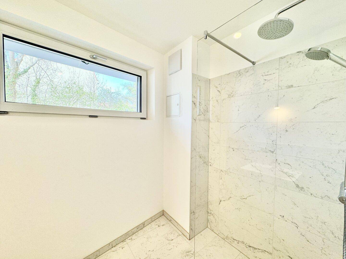 Helle Dusche mit Regenduschkopf und eleganten Marmorfliesen, gut beleuchtet durch ein Fenster.
