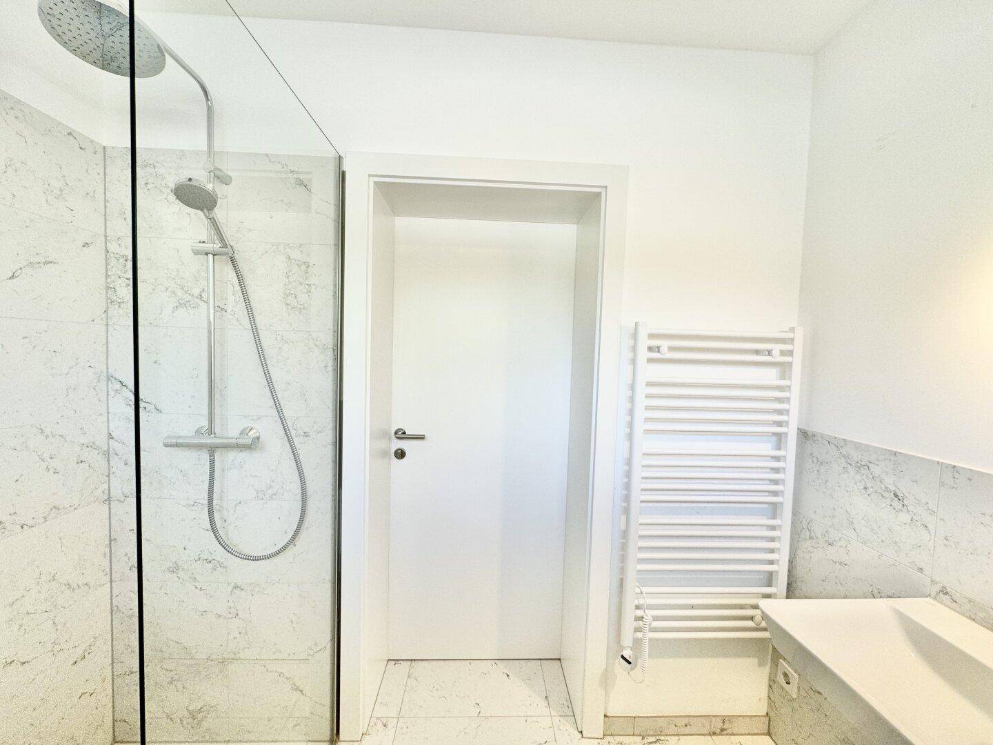 Geräumiges Badezimmer mit Dusche, beheiztem Handtuchhalter und Marmorfliesen.