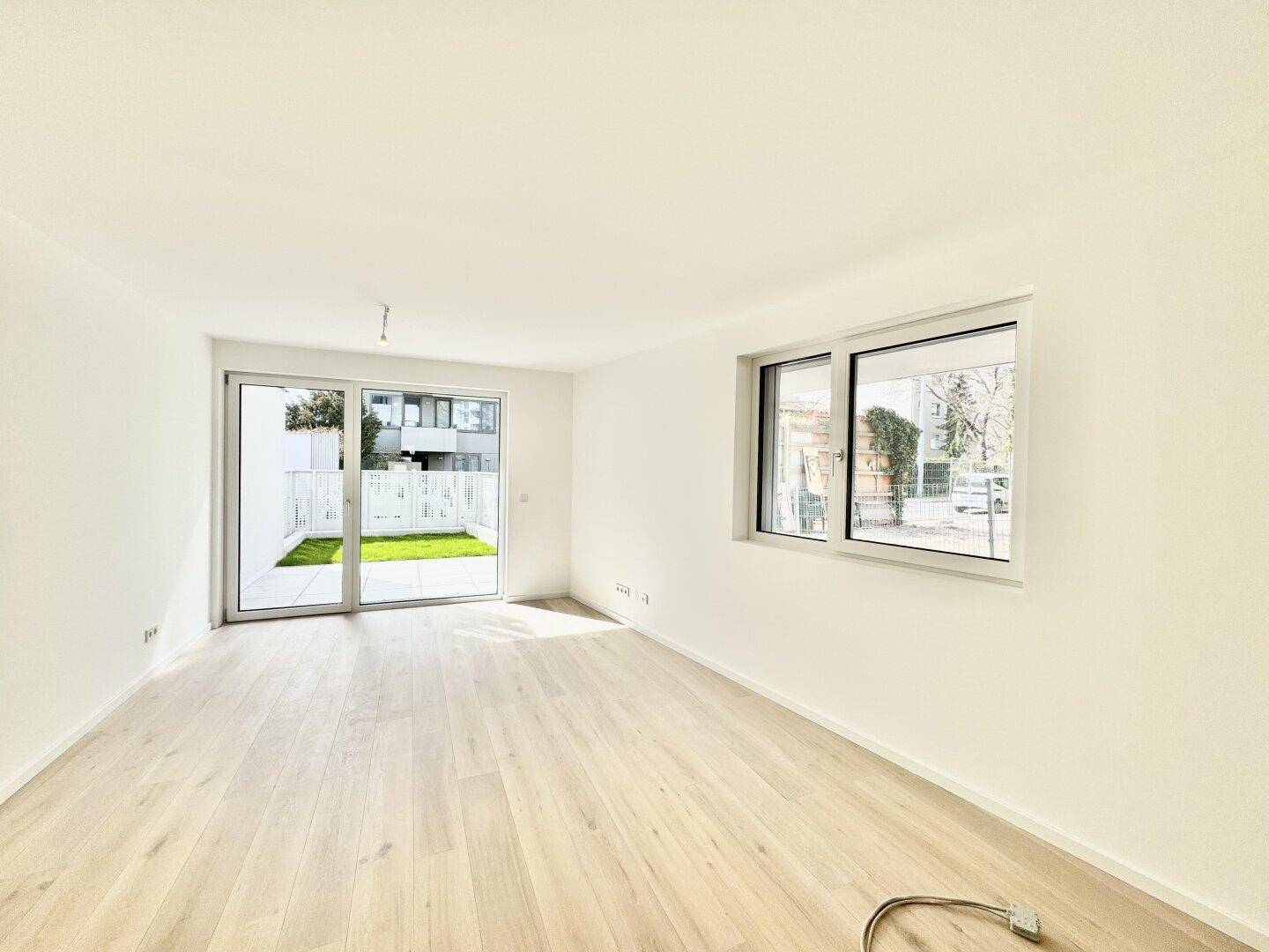 Lichtdurchfluteter Raum mit Holzboden und Schiebetür zur Terrasse mit Grünfläche.