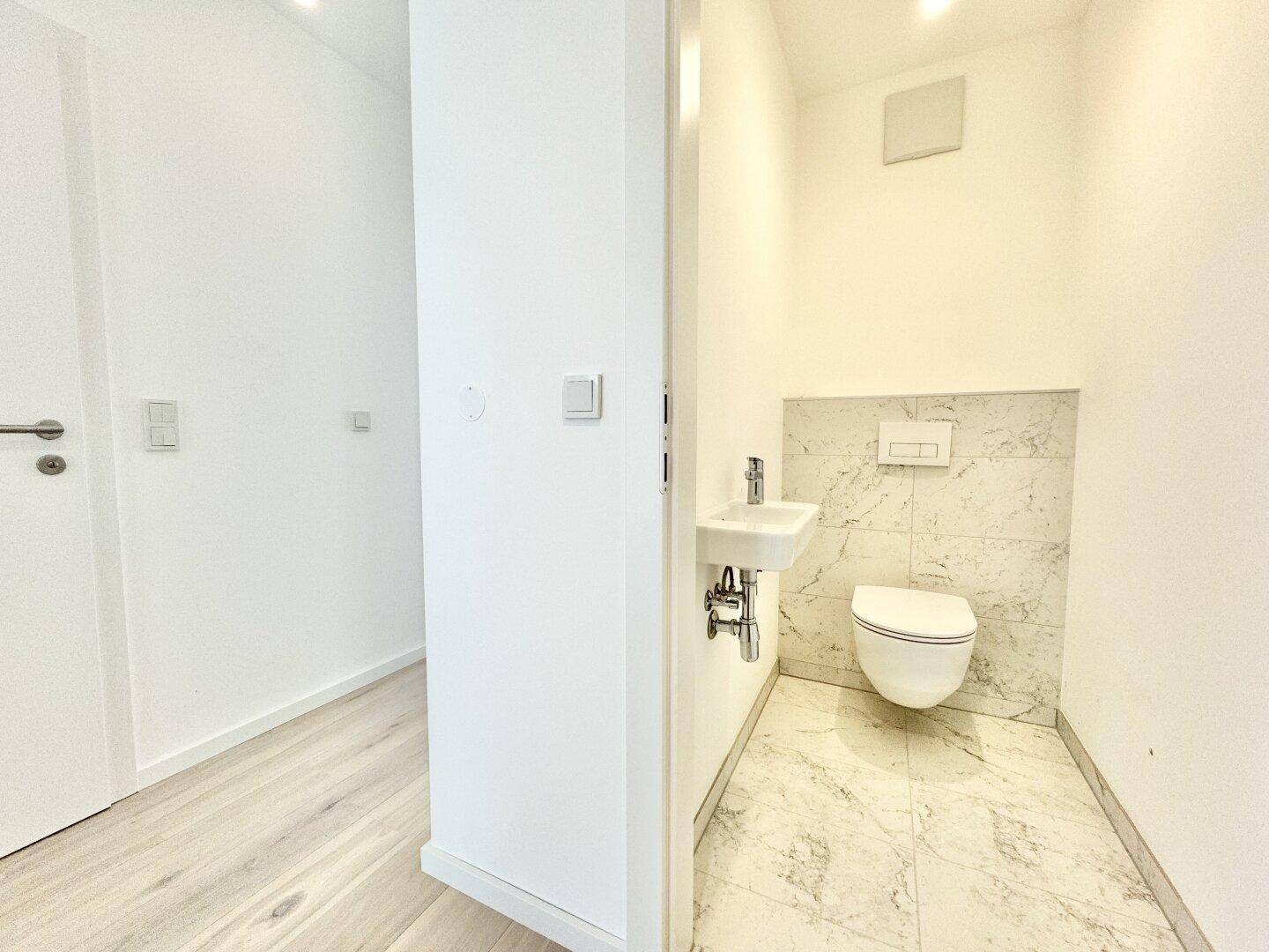Helles Gäste-WC mit wandhängender Toilette und eleganten Marmorfliesen.