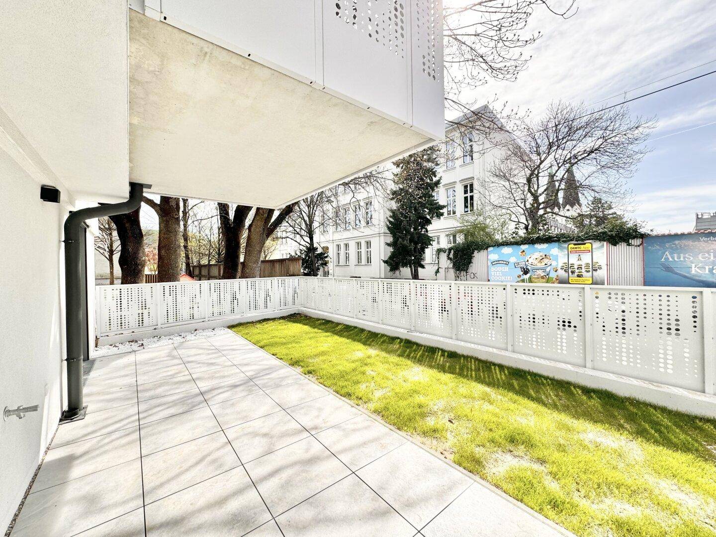 Sonniger Gartenbereich mit gepflasterter Terrasse und moderner Zaunanlage.
