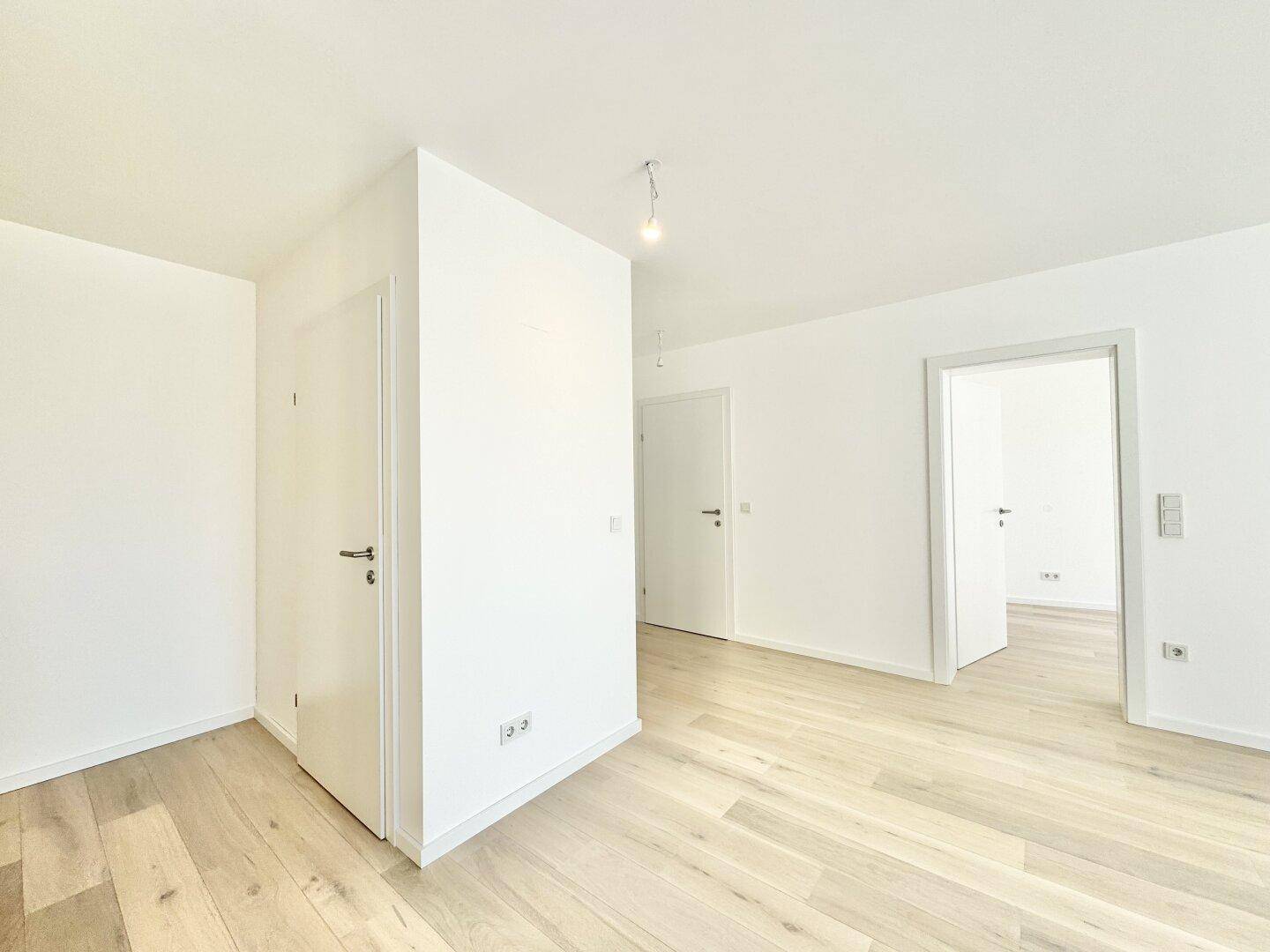 Heller, leerer Raum mit Holzboden und mehreren Türen, der verschiedene Bereiche verbindet.