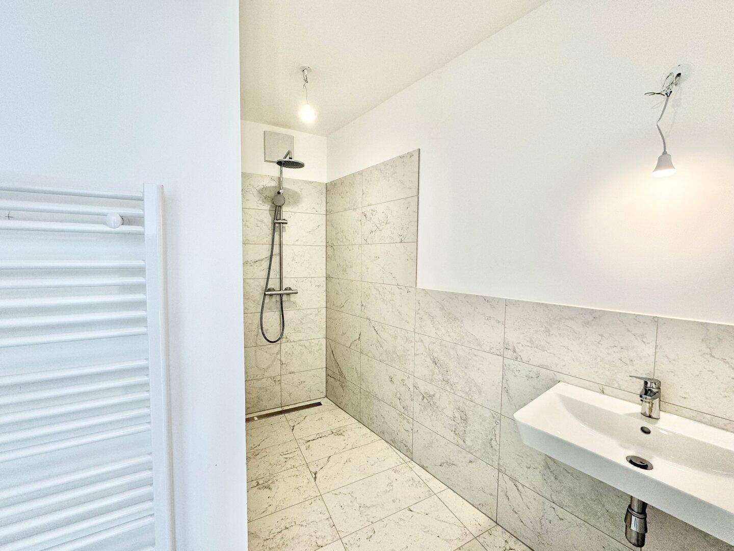 Elegantes Badezimmer mit ebenerdiger Dusche, modernem Waschbecken und Handtuchheizkörper.