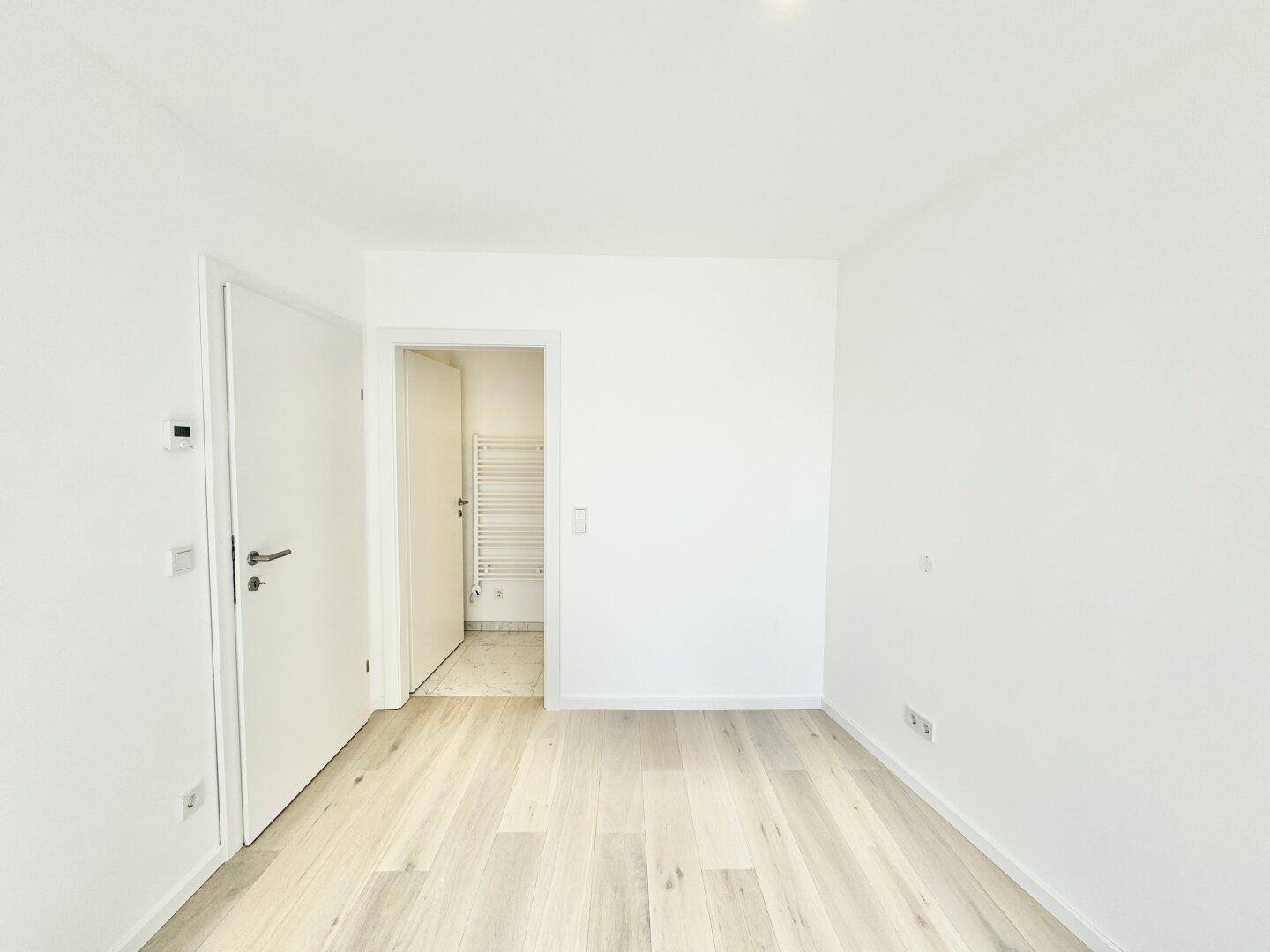Helles Schlafzimmer mit Holzboden und direktem Zugang zu einem modernen Badezimmer.