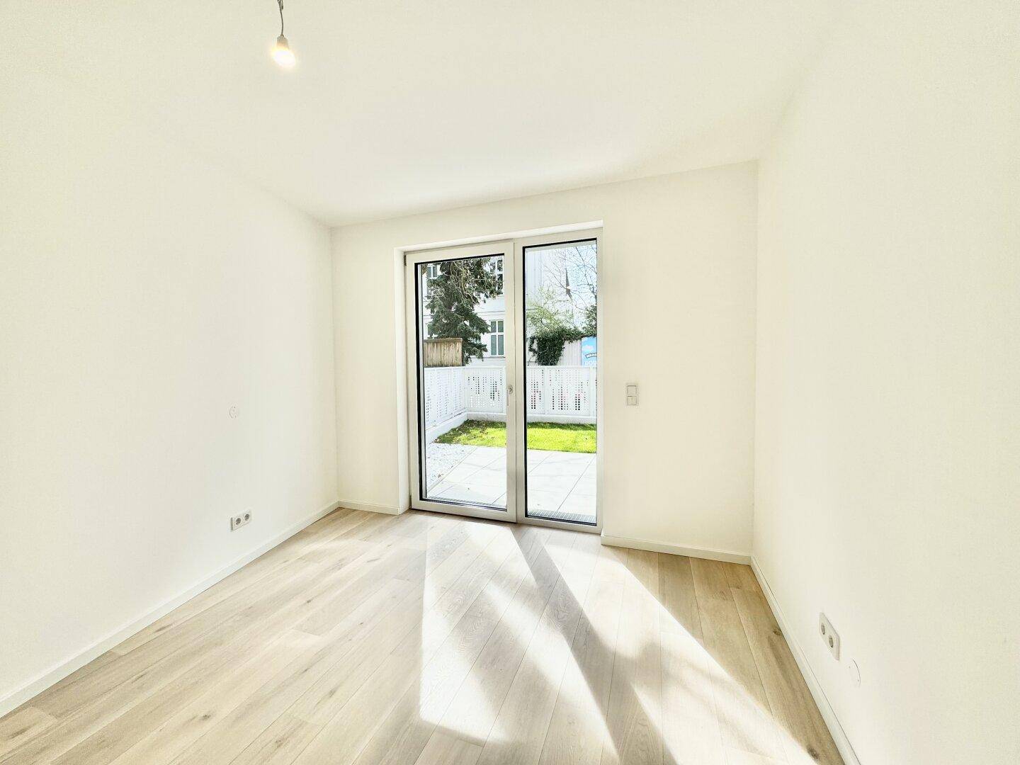 Geräumiges Schlafzimmer mit Holzboden und großen Fenstern zum privaten Garten.