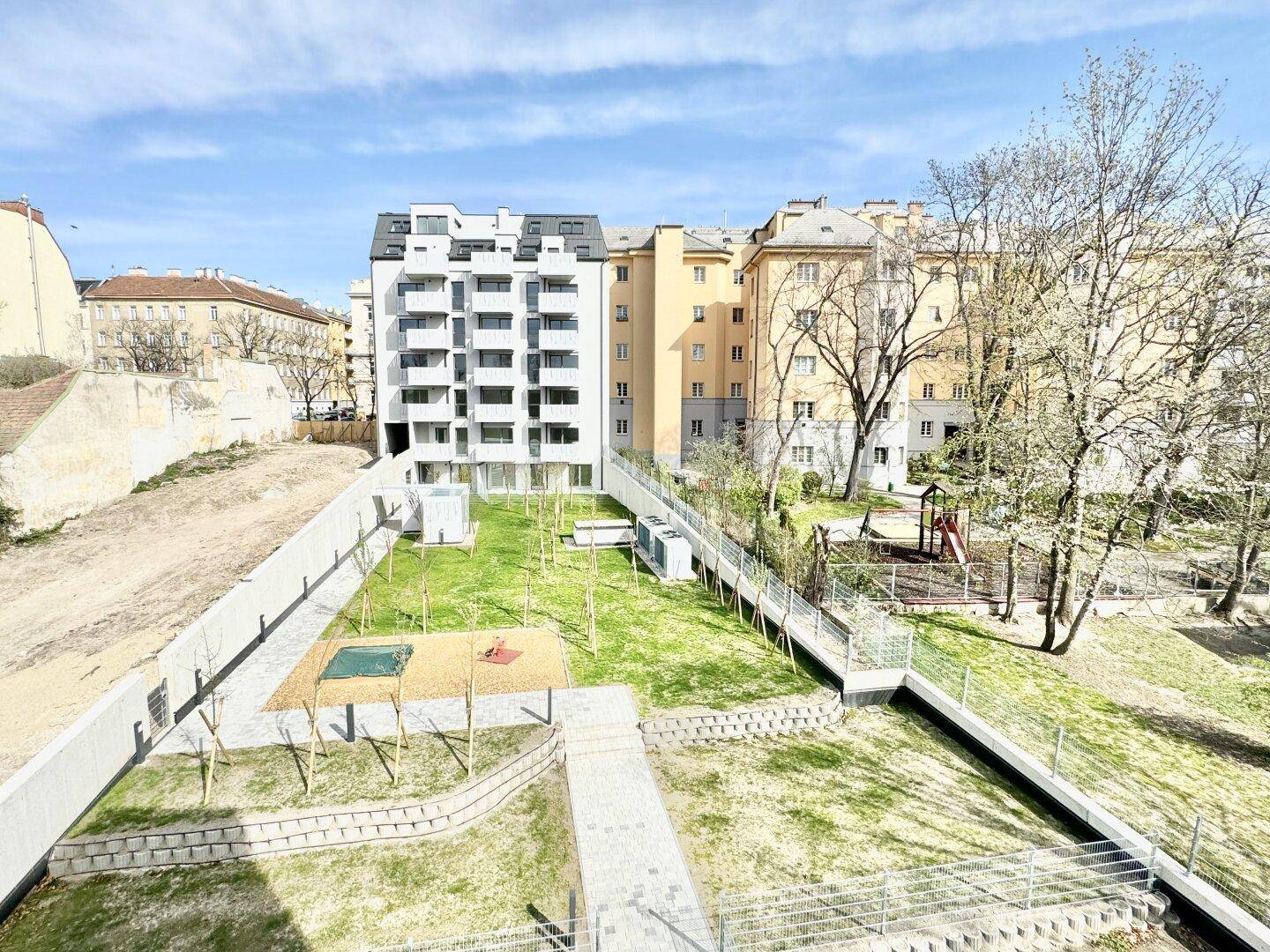 Überblick über die grüne Außenanlage mit Spielplatz und umliegenden Wohngebäuden.