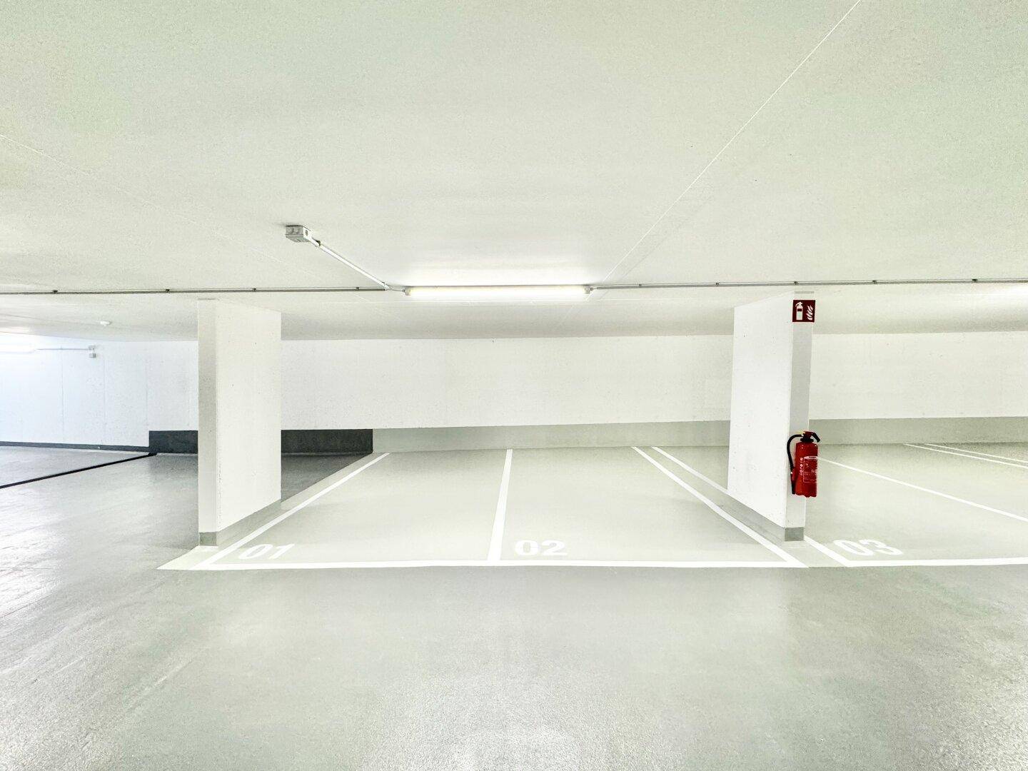 Saubere und gut beleuchtete Tiefgarage mit markierten Stellplätzen und Brandschutz.