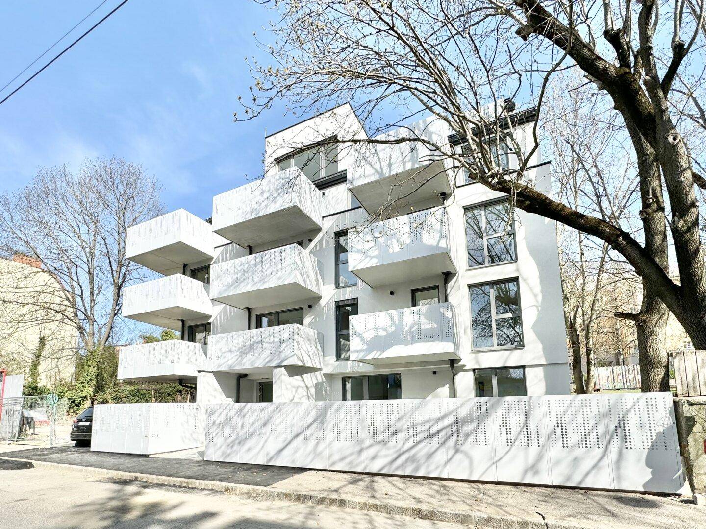 Moderne weiße Fassade eines Neubaus mit zahlreichen Balkonen und großen Fenstern.