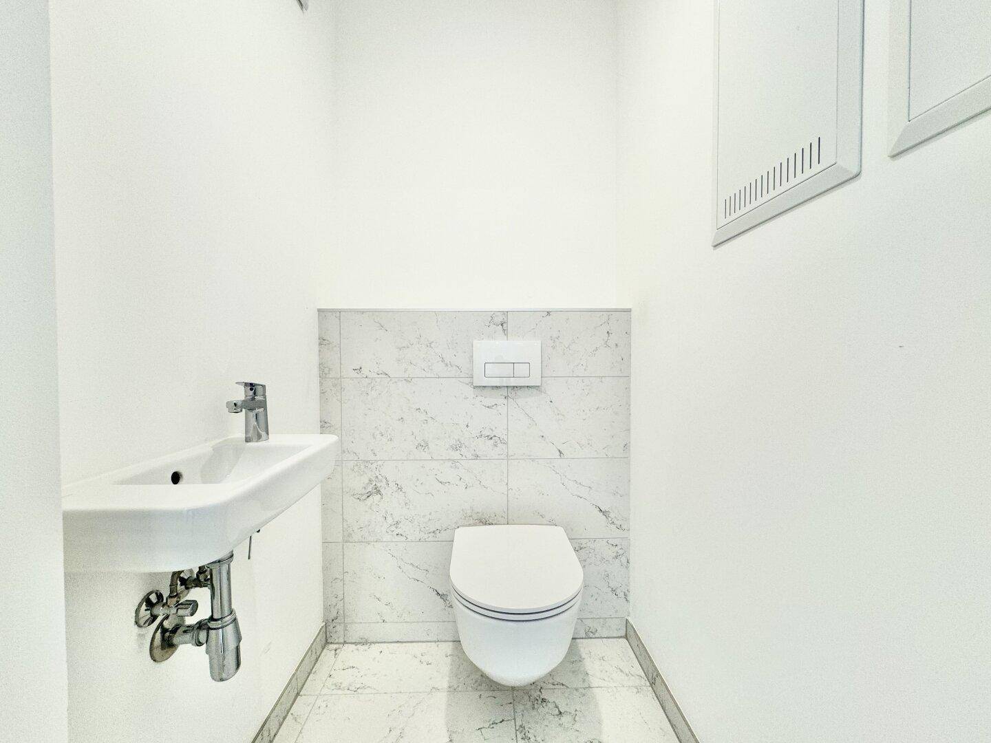 Helles Gäste-WC mit wandhängender Toilette und kleinem Waschbecken, modern gefliest.