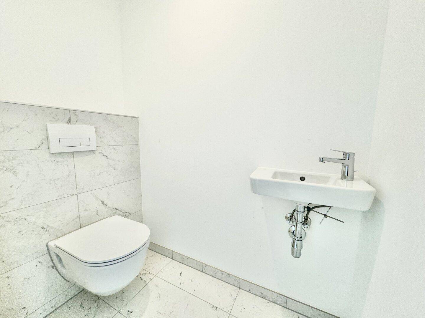 Kleines Gäste-WC mit Wand-WC und modernem Waschbecken, hell gefliest und funktional gestaltet.