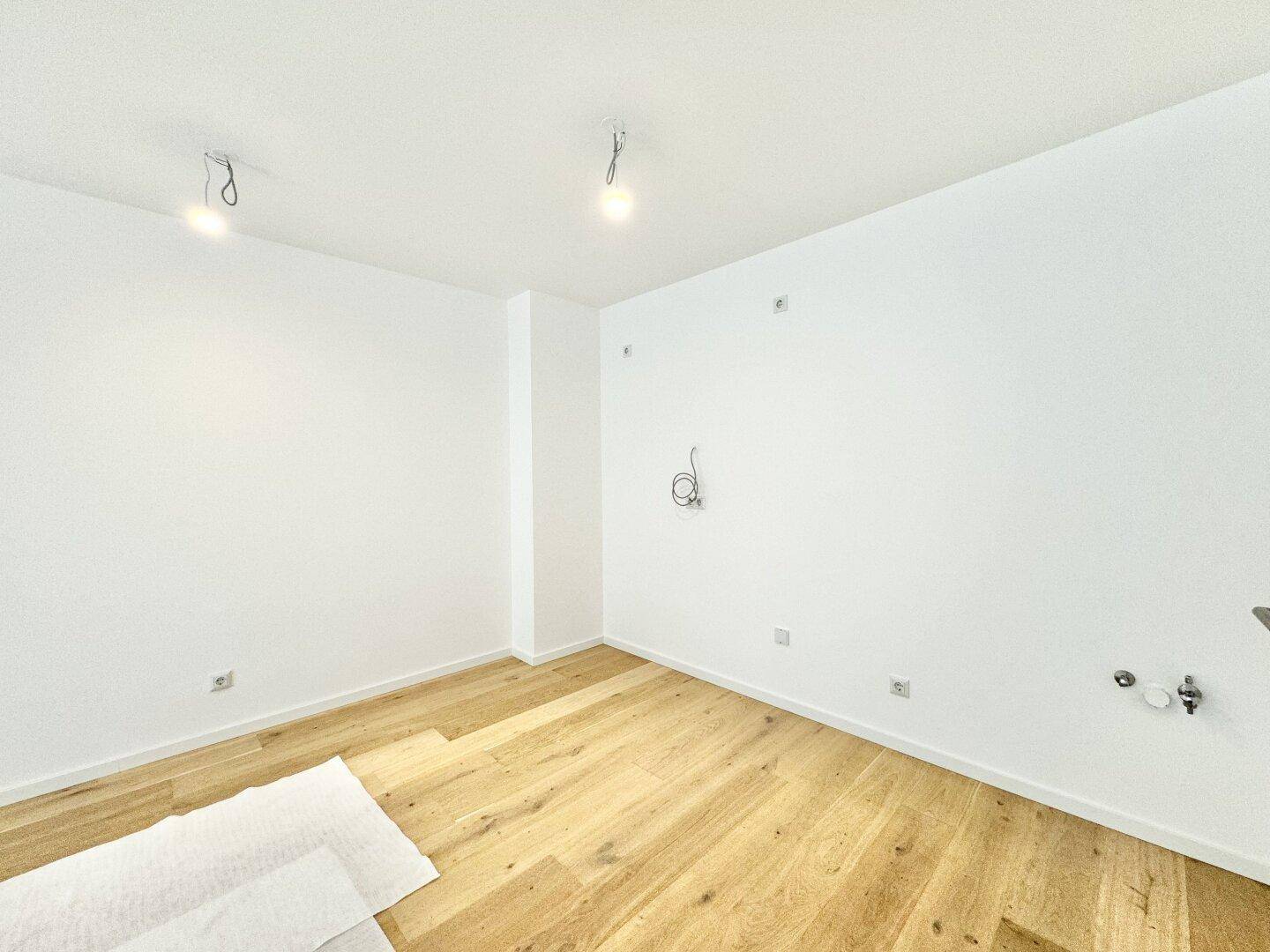 Leerer Raum mit Holzboden und weißen Wänden, vorbereitet für die Installation einer Küche.