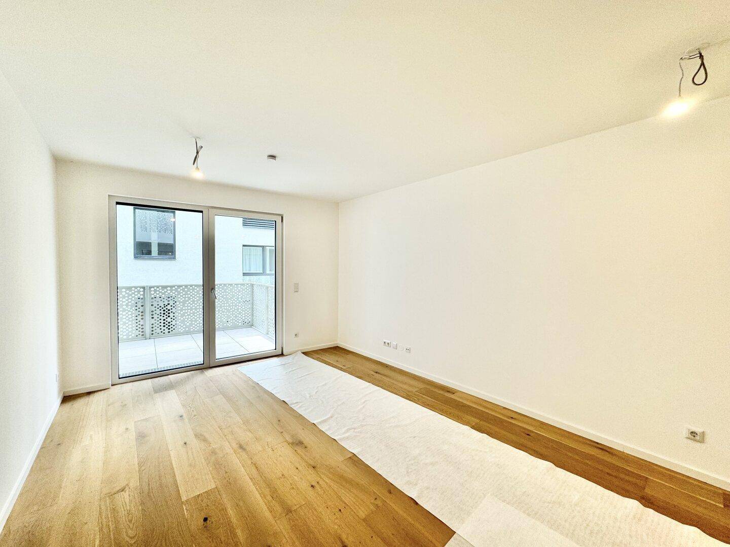 Helles Wohnzimmer mit Holzboden und großem Zugang zum Balkon, ideal für natürliches Licht.