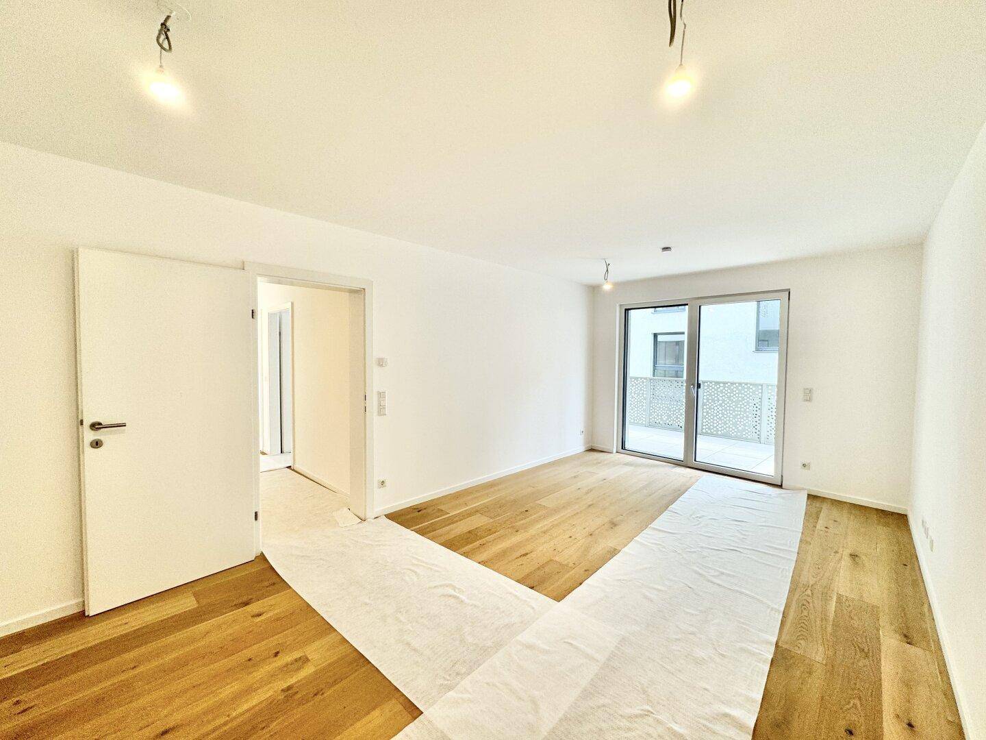 Geräumiges Wohnzimmer mit Holzboden, Balkonzugang und Verbindung zu einem weiteren Raum.