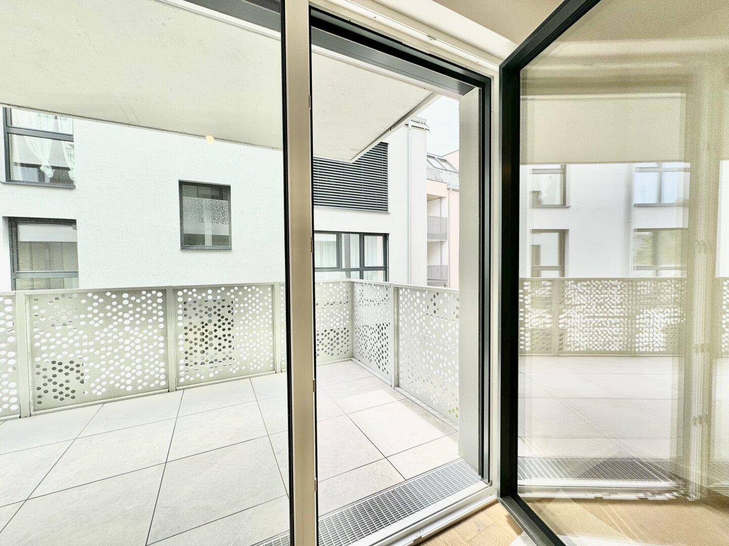 Blick vom Innenraum auf den modernen Balkon mit perforiertem Geländer und Fliesenboden.