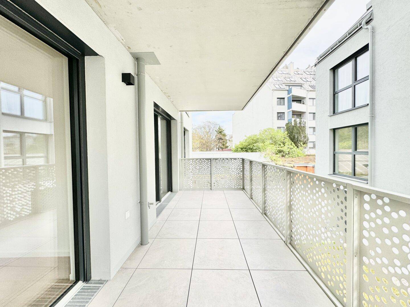 Geräumiger Balkon mit Fliesenboden, modernem Geländer und Blick ins Grüne.