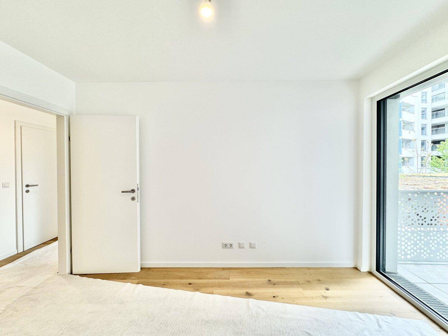 Schlafzimmer mit Holzboden, Zugang zum Balkon und viel natürlichem Licht durch die große Tür.