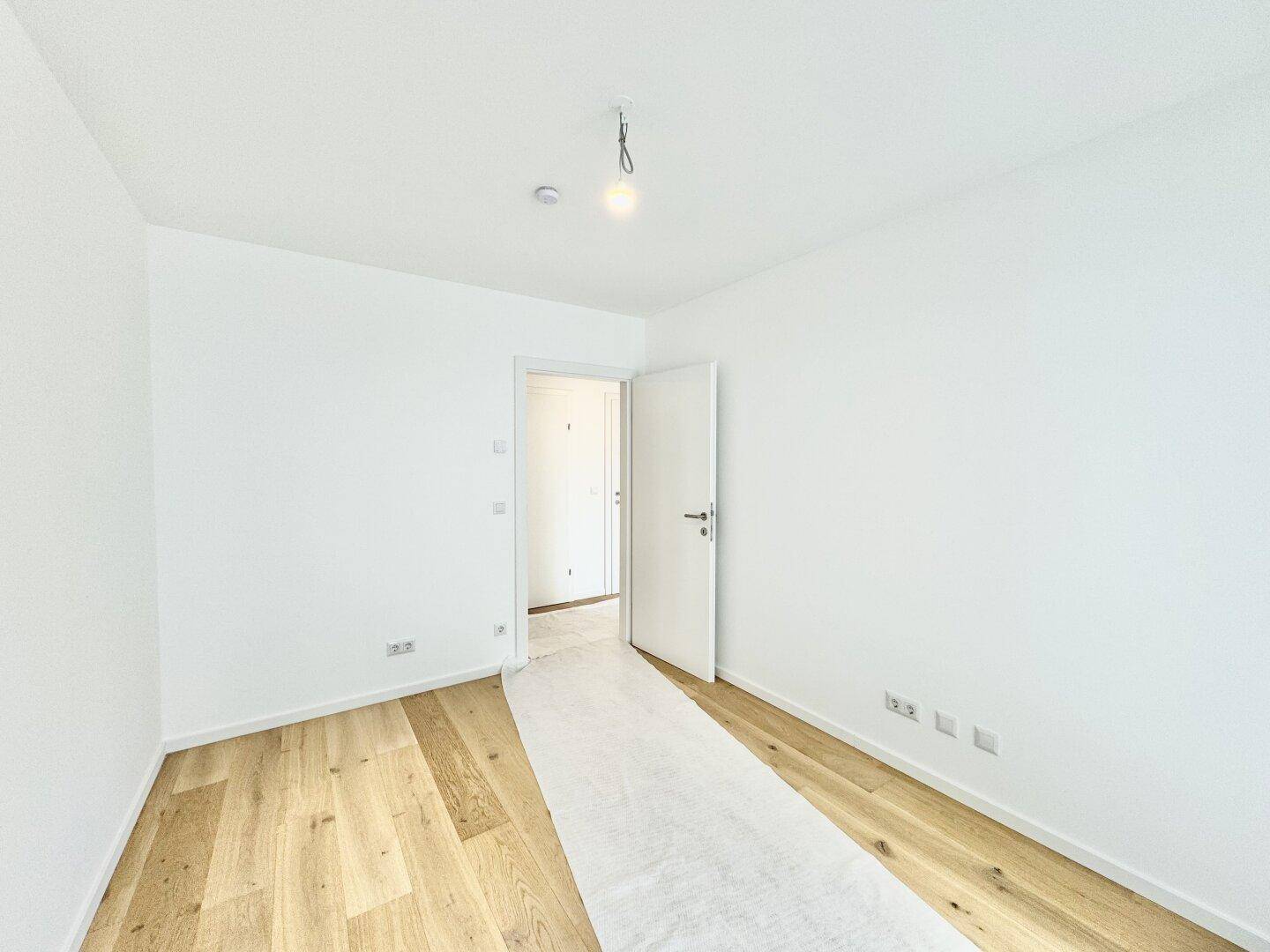 Helles Schlafzimmer mit Holzboden und weiß gestrichenen Wänden, bereit zur individuellen Gestaltung.