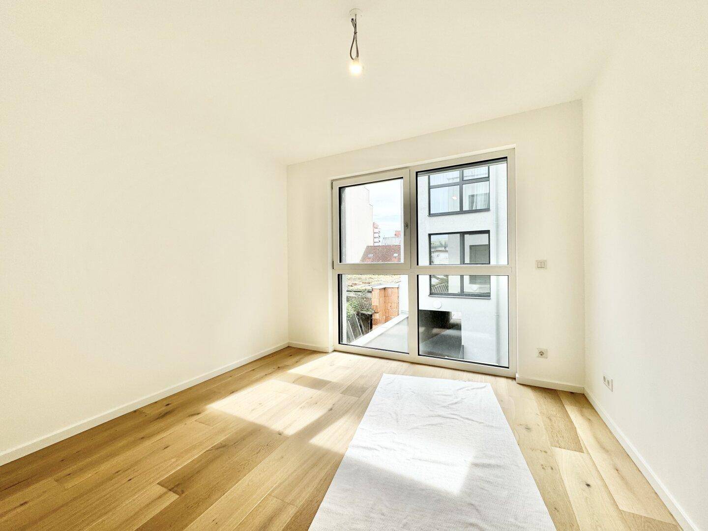 Schlafzimmer mit großem Fenster für viel Tageslicht und Holzboden, unmöbliert und hell.
