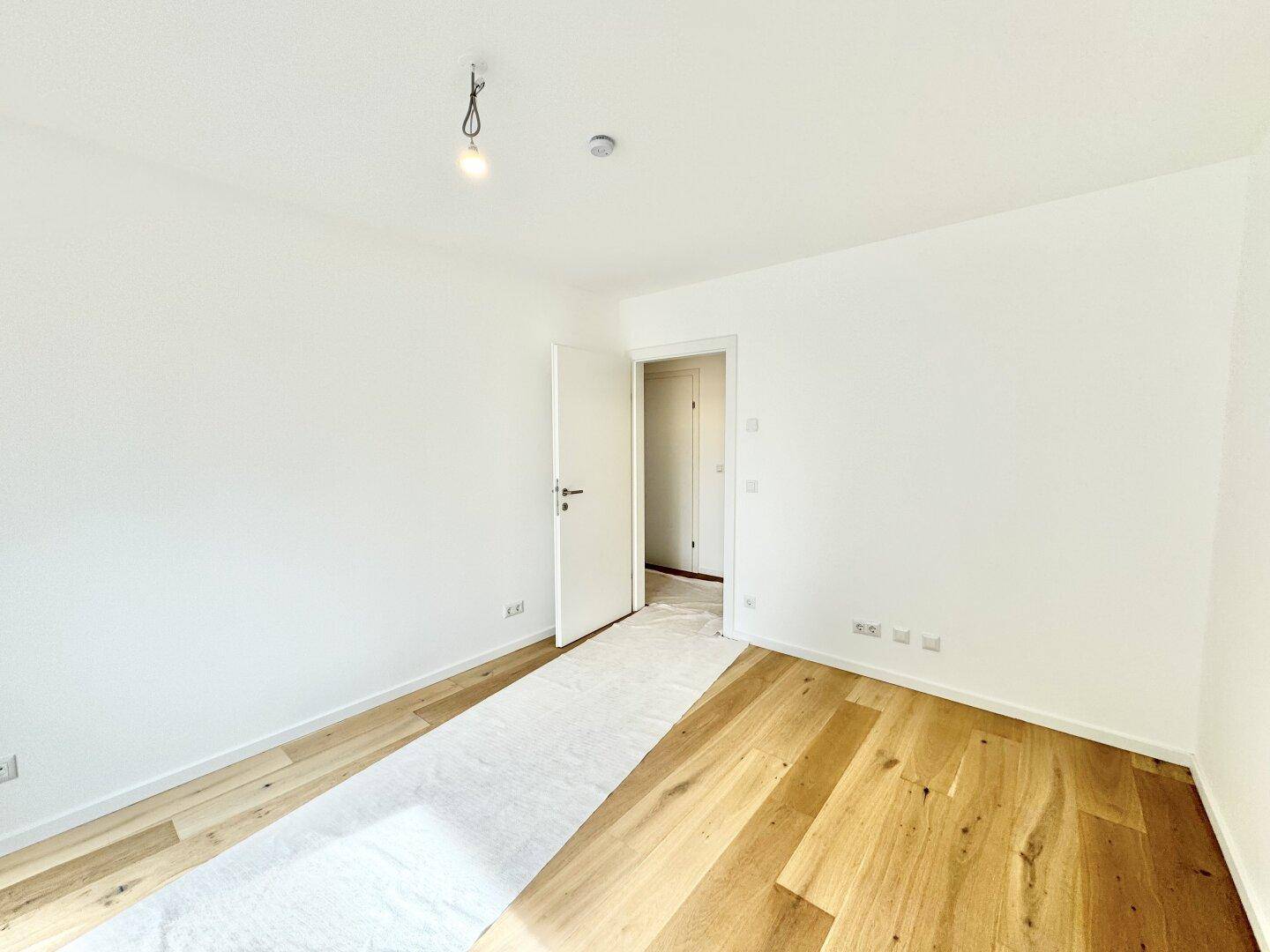 Geräumiges Schlafzimmer mit Holzboden und weiß gestrichenen Wänden, ideal für individuelle Einrichtung.