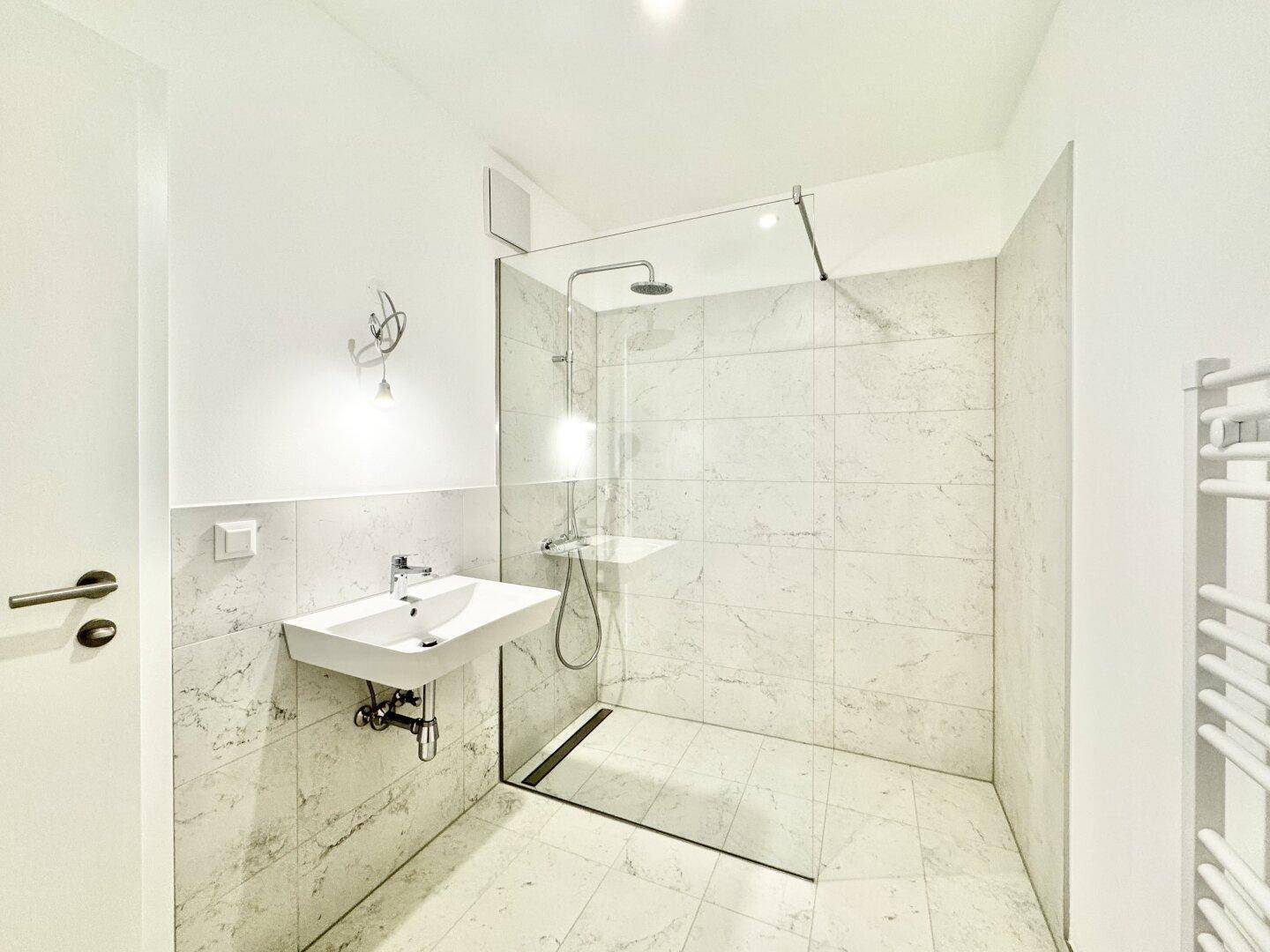 Modernes Badezimmer mit ebenerdiger Dusche, weißen Fliesen und einem Heizkörper für Handtücher.