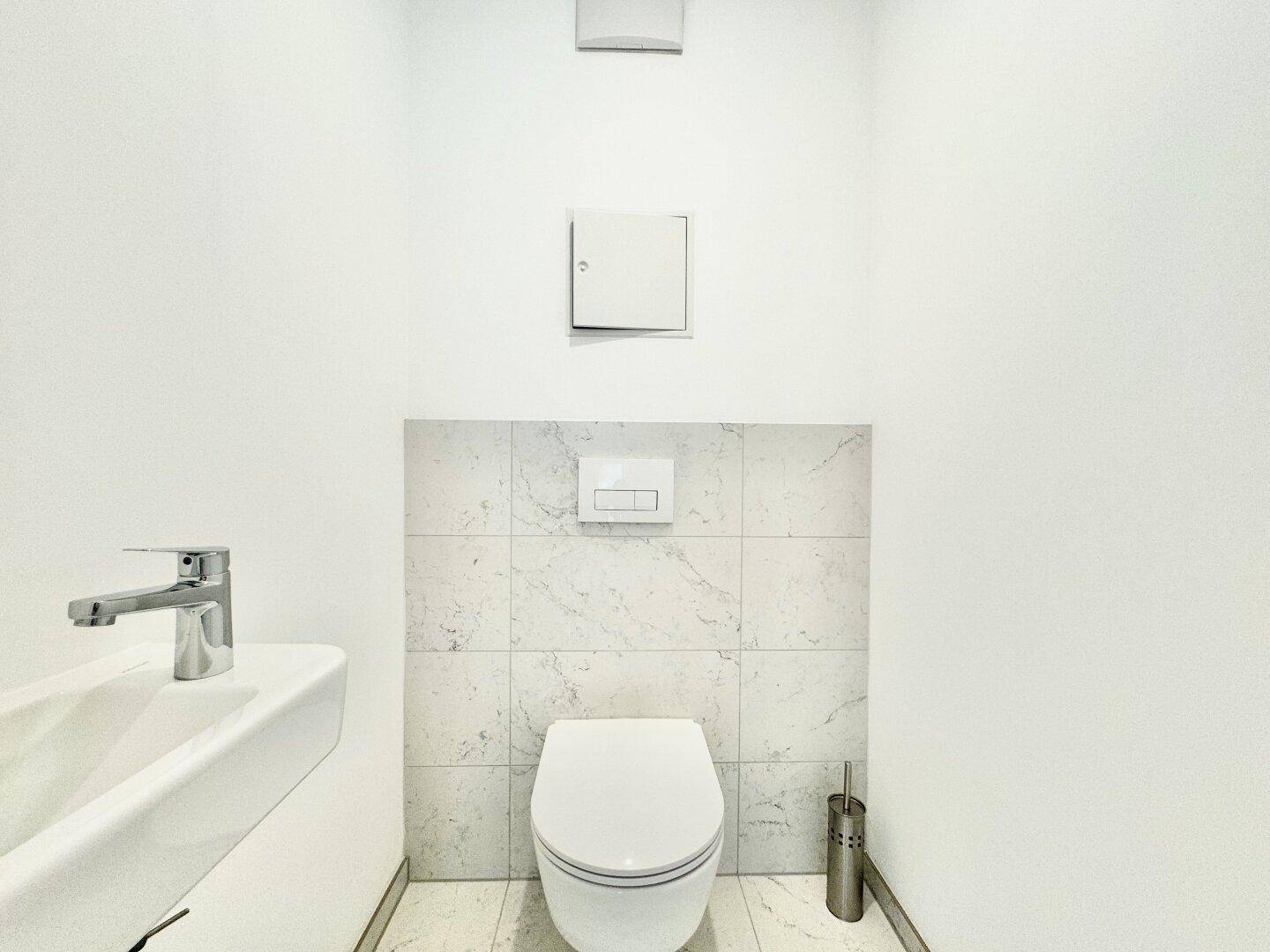 Modernes Gäste-WC mit wandhängender Toilette und kleinem Waschbecken, hell gefliest.