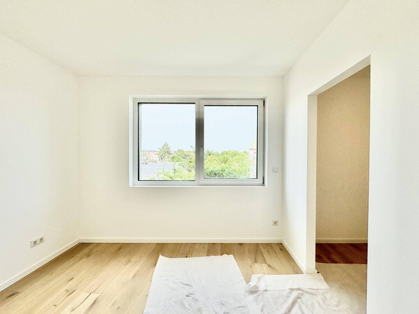 Leeres Zimmer mit hellem Eichenparkettboden und großem Fenster für viel Tageslicht.