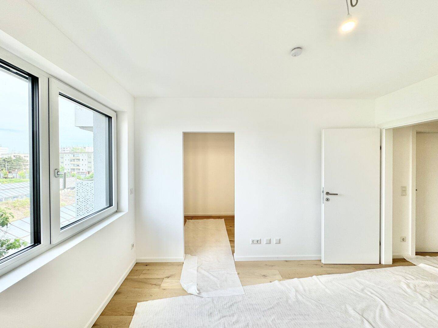 Geräumiges Zimmer mit Holzboden und Fenster, das viel natürliches Licht hereinlässt.