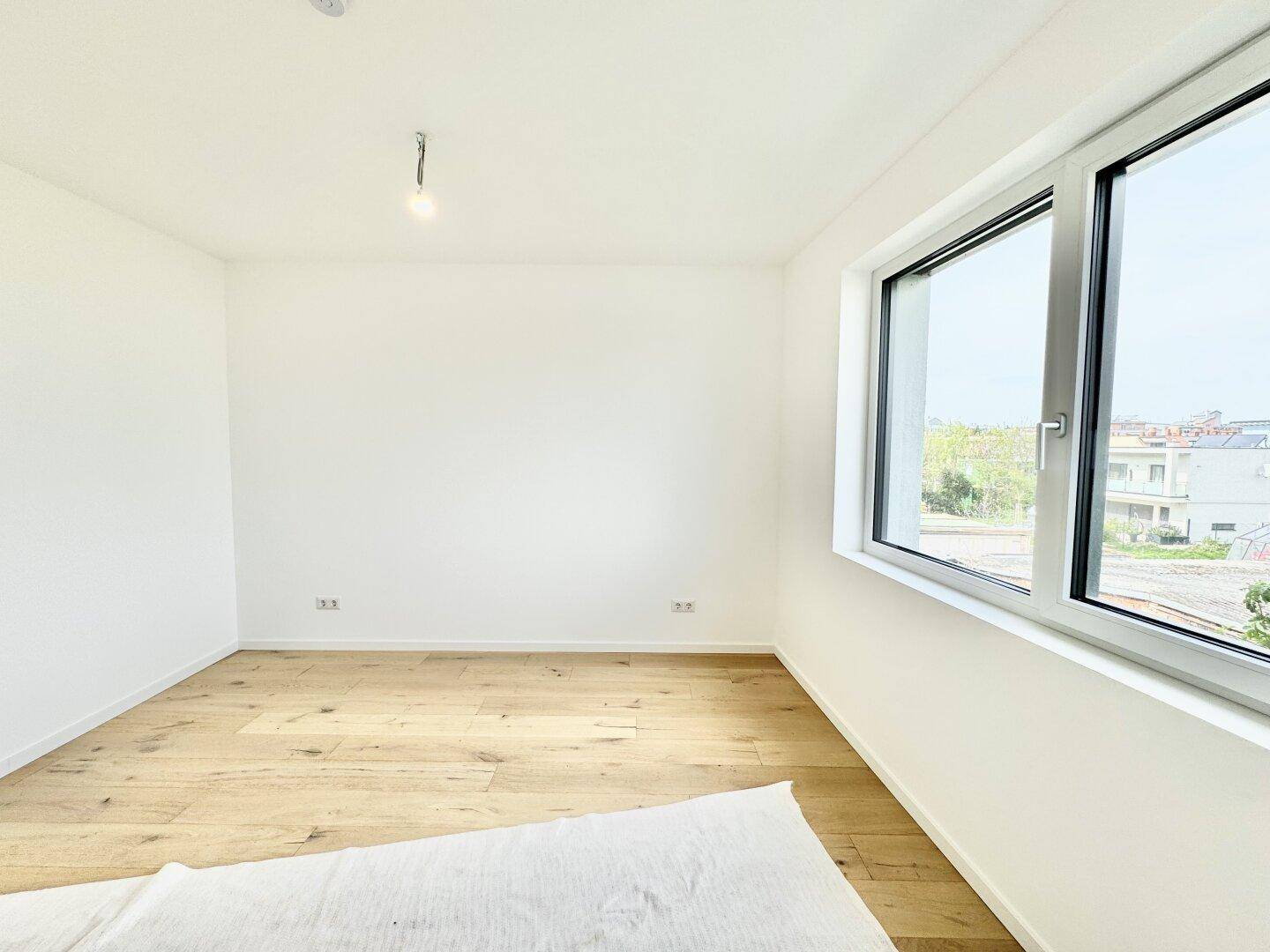 Helles Zimmer mit Eichenparkettboden und großem Fenster, bereit zum Einrichten.