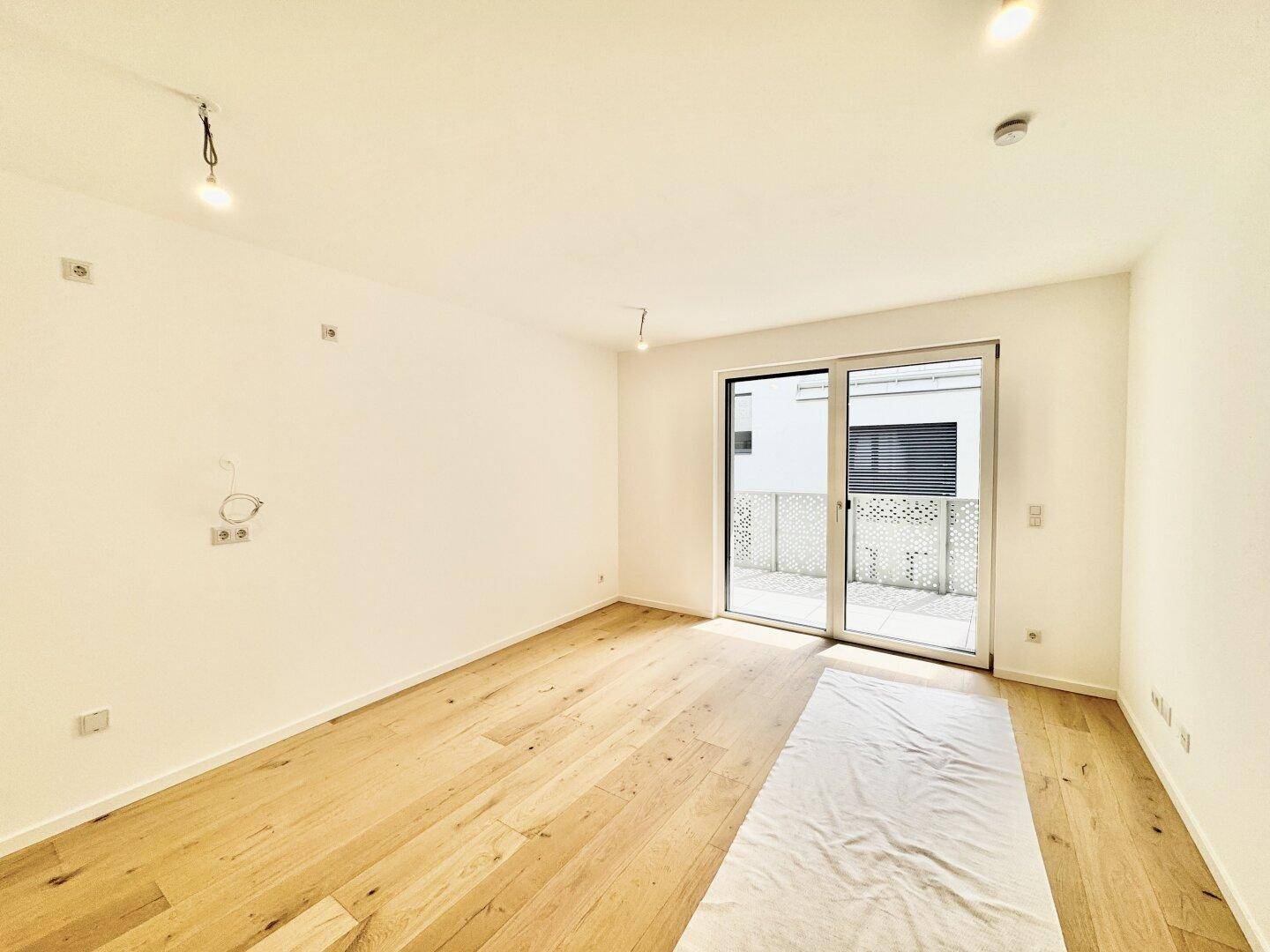 Geräumiges Wohnzimmer mit Holzboden und Schiebetür zum sonnigen Balkon.