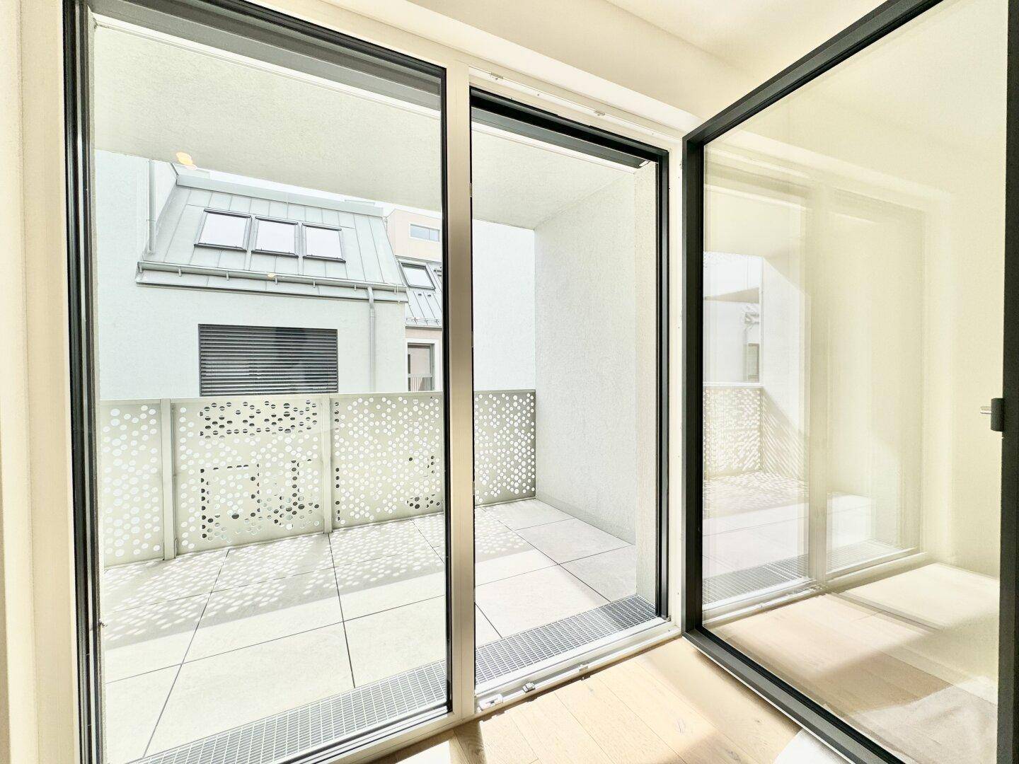 Blick aus dem Wohnzimmer auf den modernen Balkon mit perforiertem Geländer.