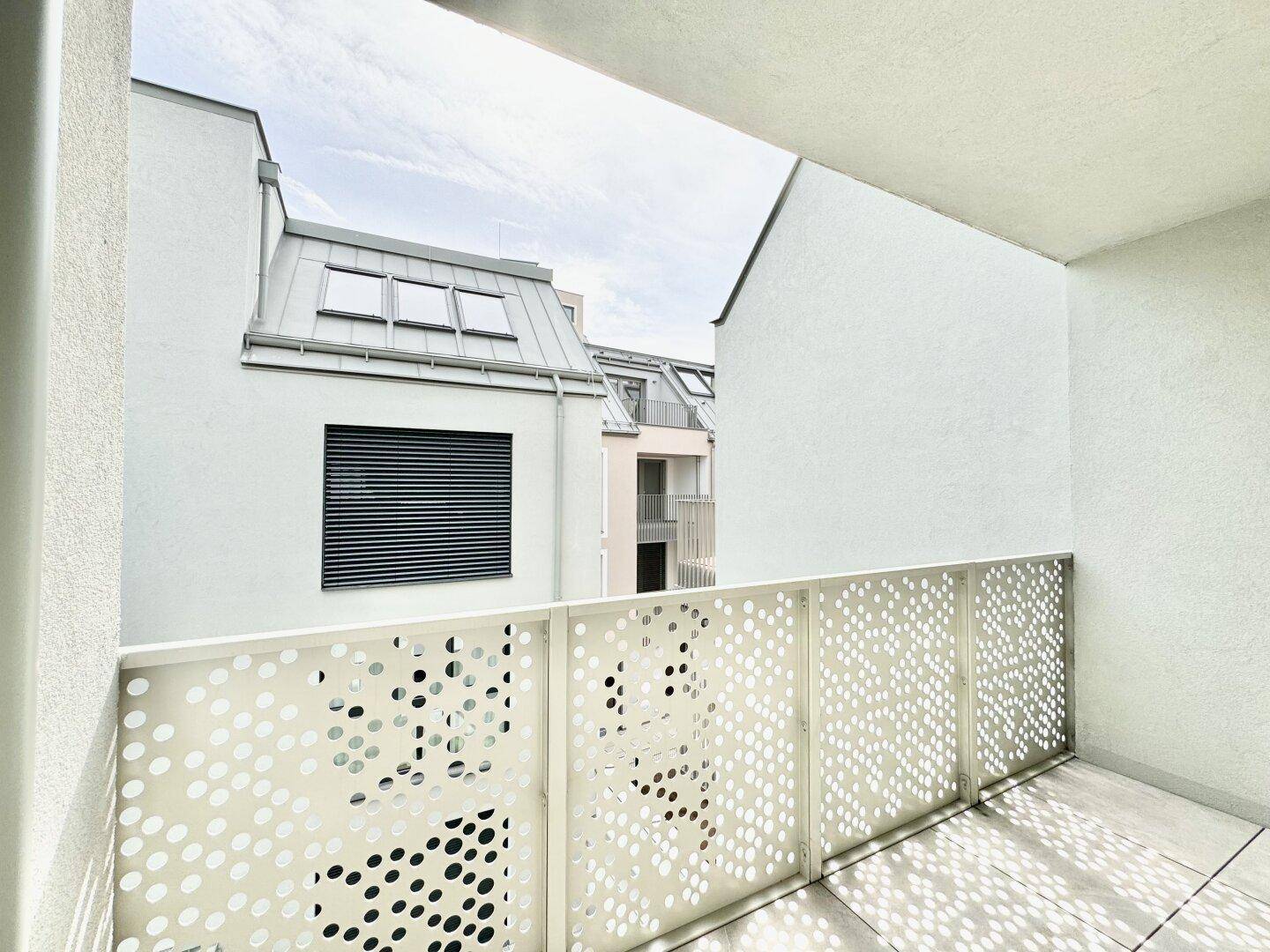 Moderner Balkon mit Lochblechgeländer und Blick auf die umliegende Architektur.