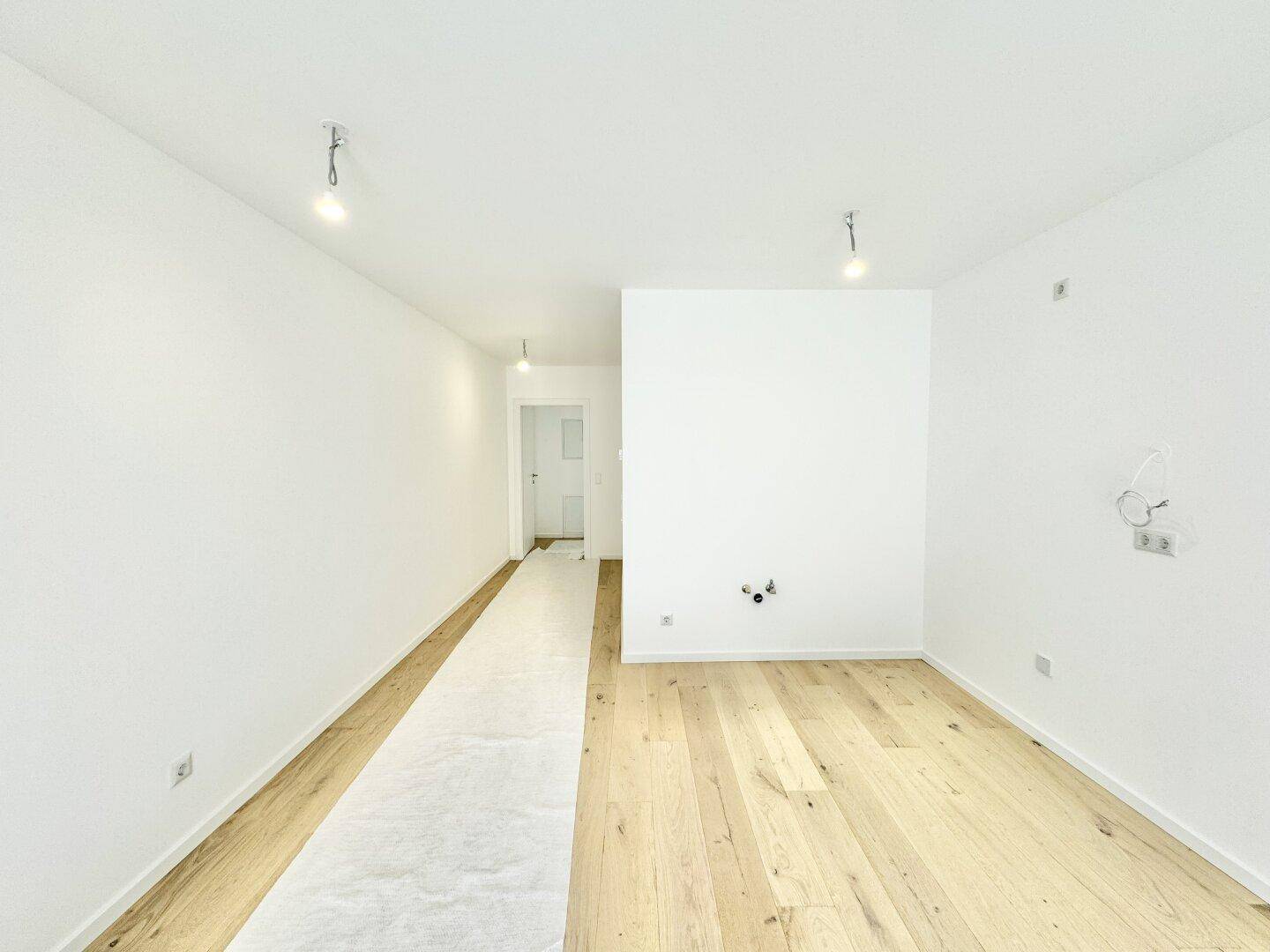 Geräumiger, heller Raum mit Eichenparkettboden und weißen Wänden, unmöbliert.