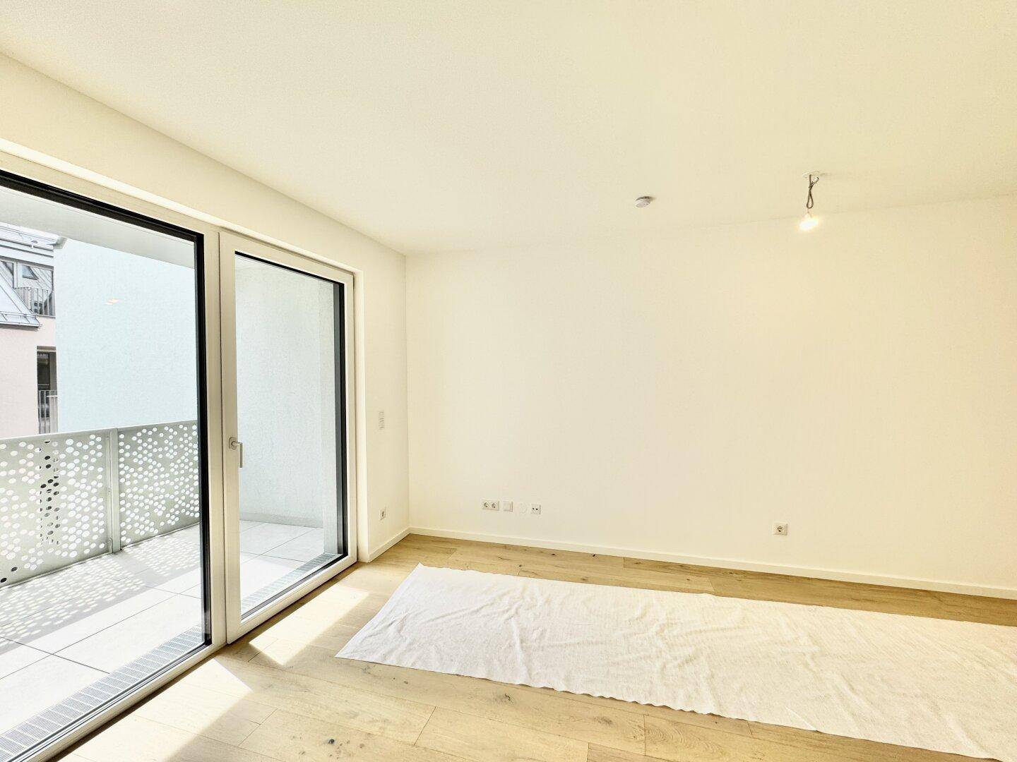 Helles Zimmer mit Holzboden und großer Schiebetür zum Balkon, sonnendurchflutet.