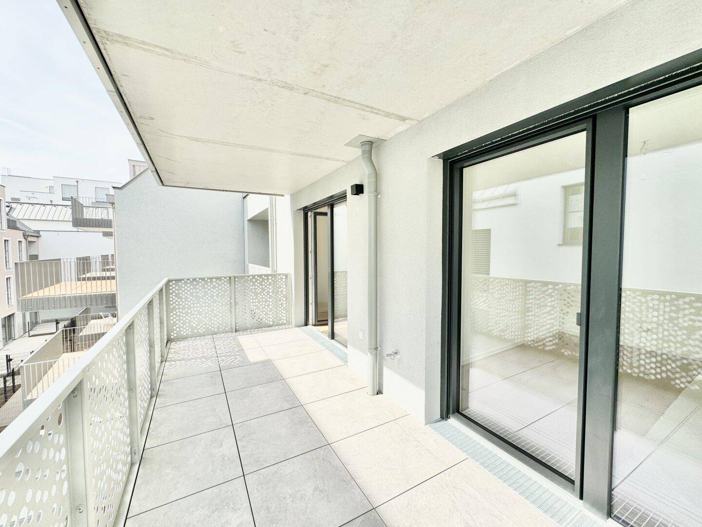 Heller Balkon mit großen Schiebetüren, die Zugang zu einem Innenraum bieten, und moderner Architektur.