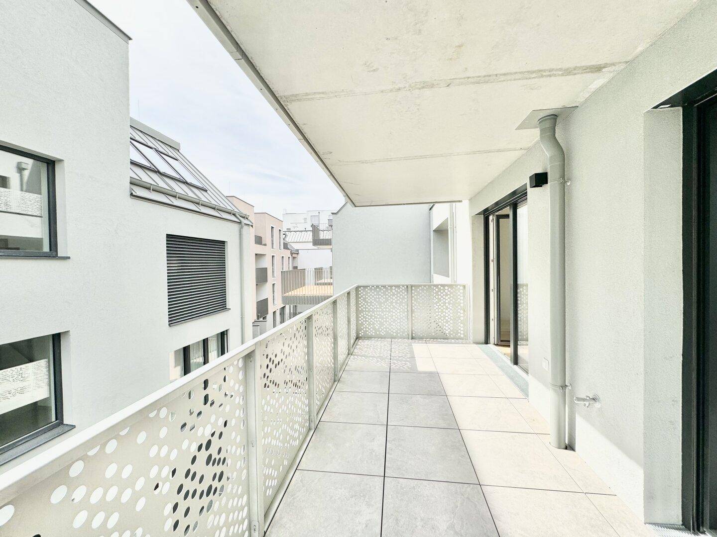 Langer Balkon mit modernem Design, Fliesenboden und Blick auf die umliegende Wohnbebauung.