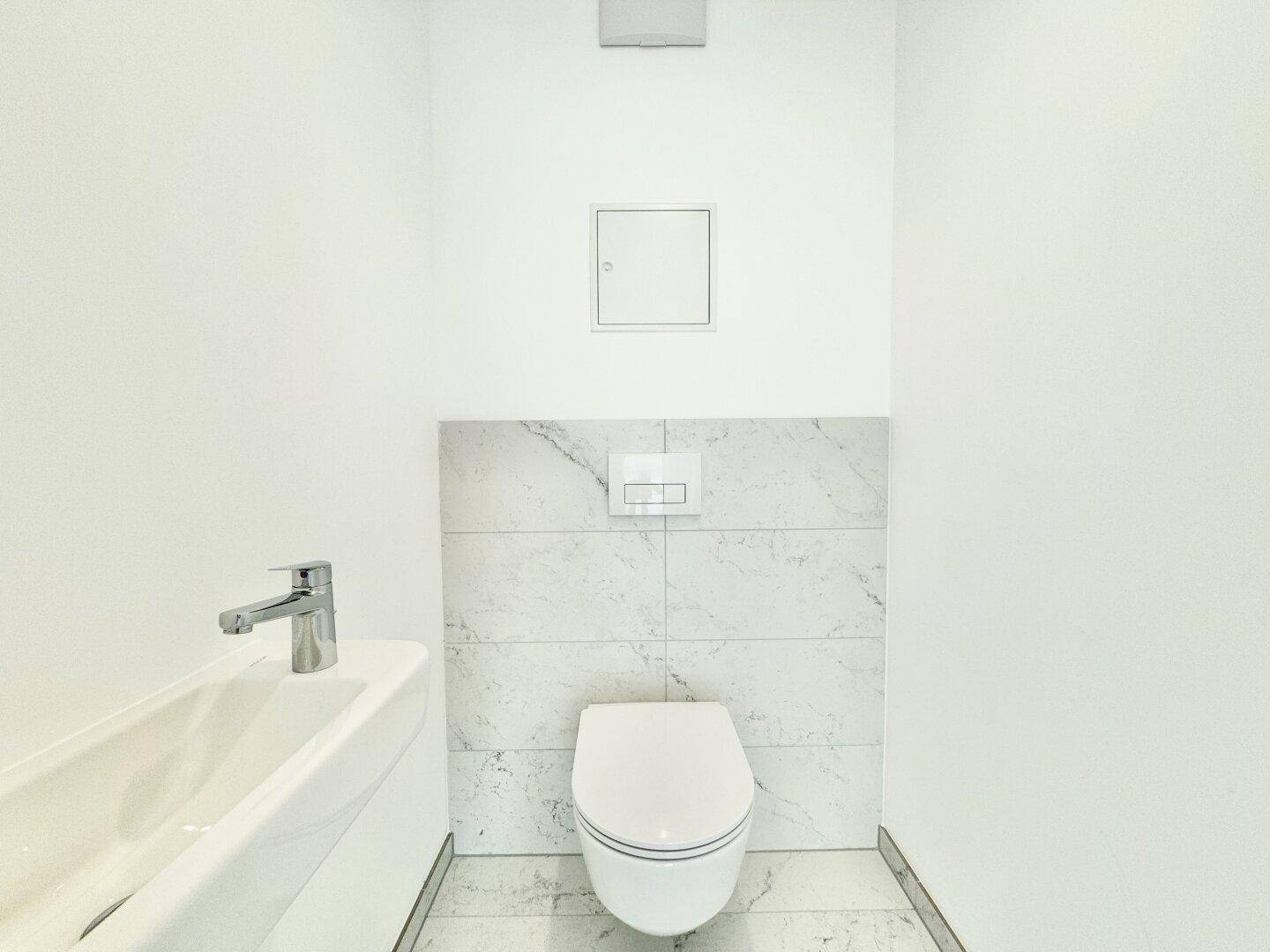 Modernes Gäste-WC mit wandhängender Toilette, kleinem Waschbecken und Marmoroptik-Fliesen.