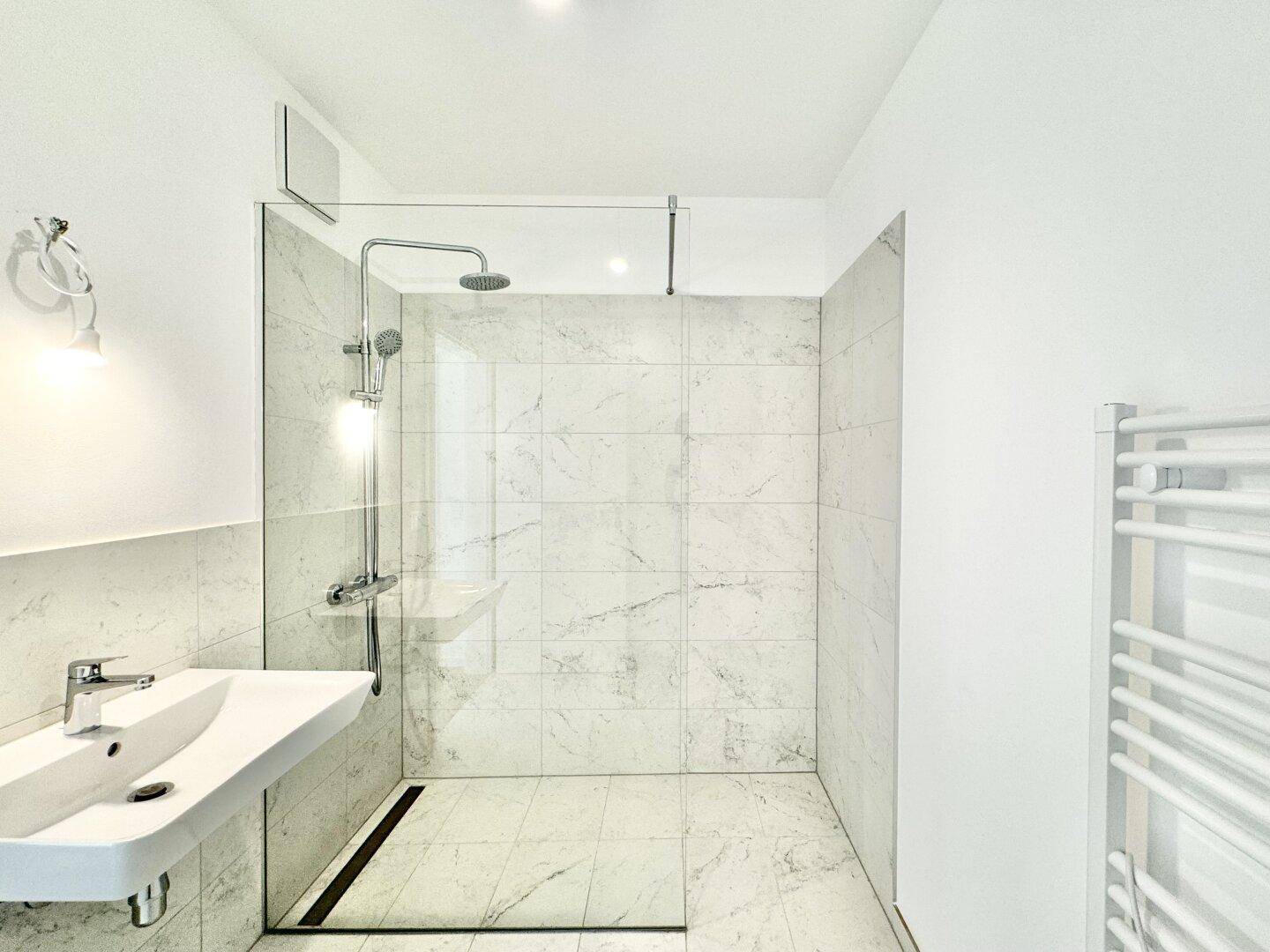 Modernes Badezimmer mit ebenerdiger Dusche, eleganten Marmoroptik-Fliesen und einem Waschbecken.