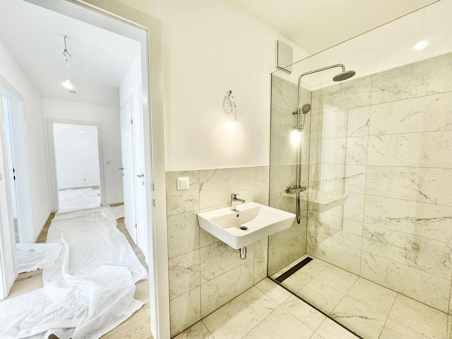 Helles Badezimmer mit moderner ebenerdiger Dusche, Waschbecken und Zugang vom Flur.
