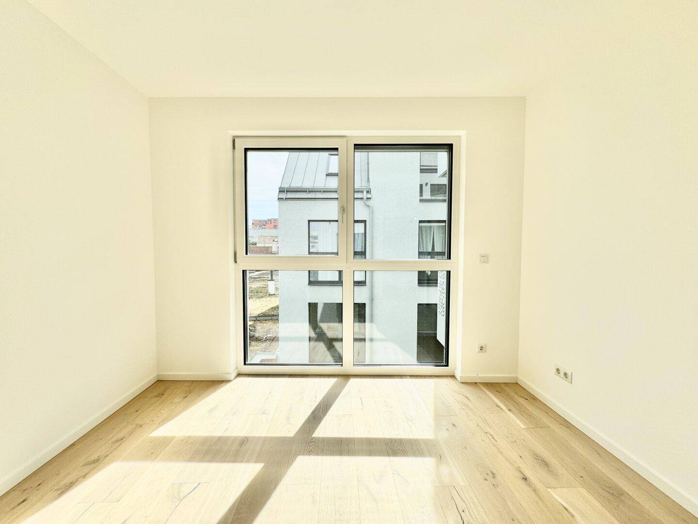 Lichtdurchfluteter Raum mit Holzboden und großem Fenster, das viel Tageslicht hereinlässt.