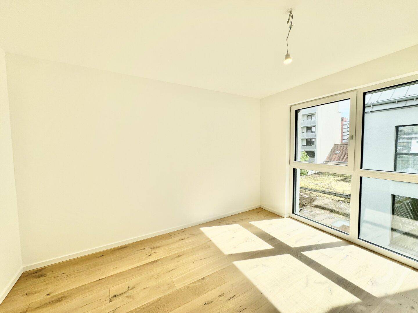 Heller Raum mit Holzboden und großem Fenster, das einen angenehmen Blick ins Grüne bietet.