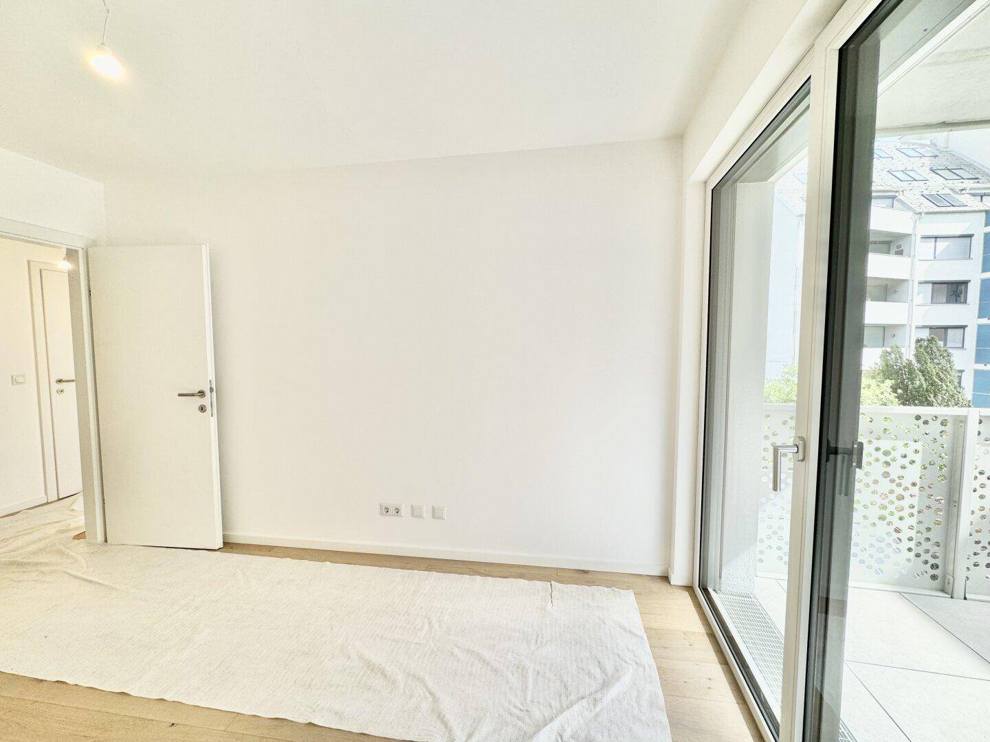 Heller Raum mit Holzboden und weißen Wänden, mit Blick auf die Umgebung durch das Fenster.