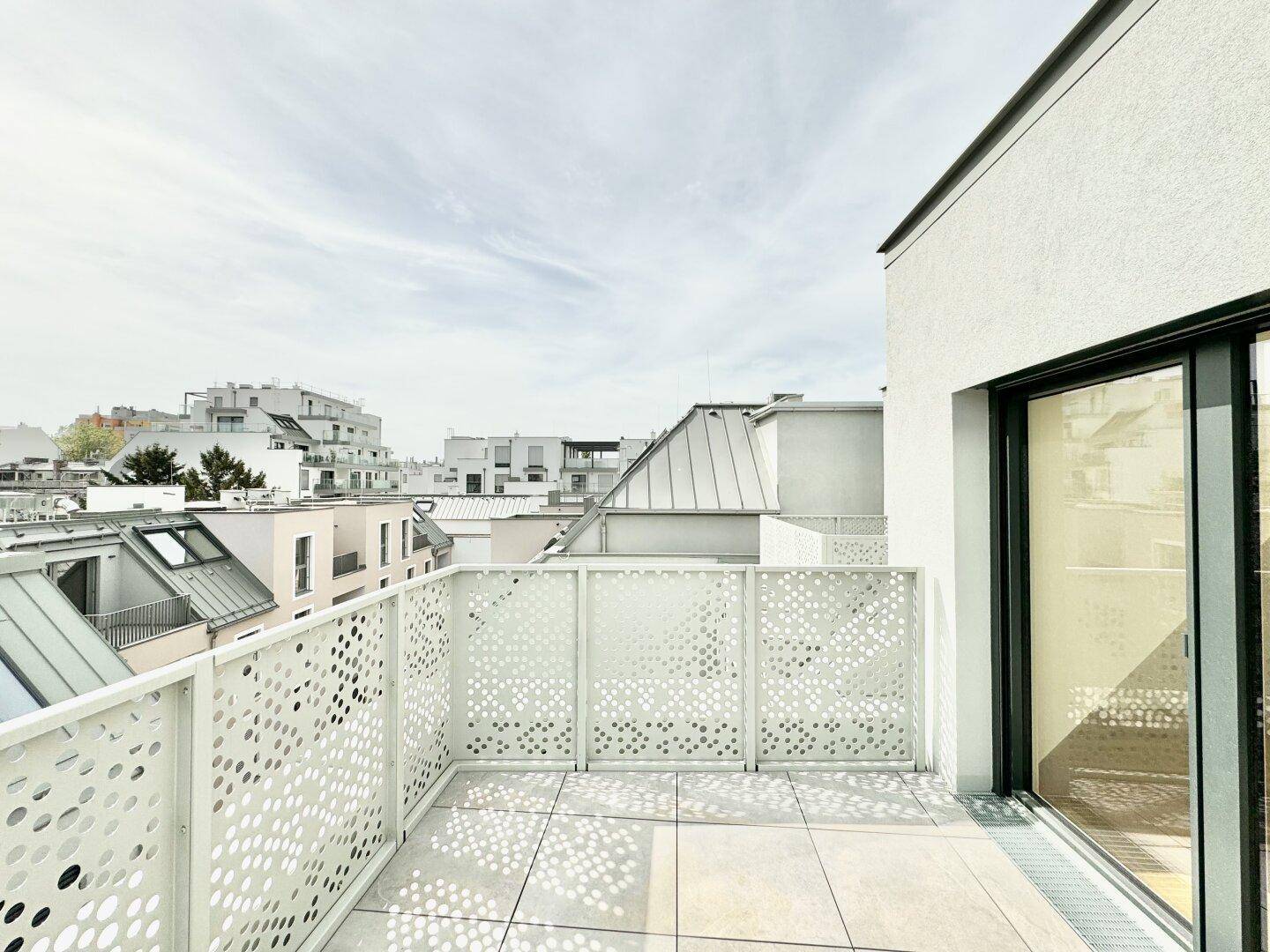 Heller Balkon mit Fliesenboden und moderner Brüstung, angrenzend an die weiße Gebäudefassade.