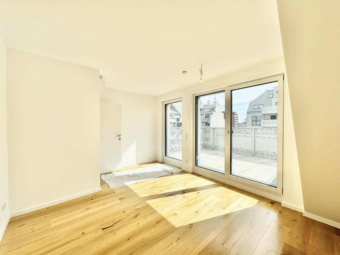 Lichtdurchfluteter Raum mit Holzboden und mehreren großen Fenstern zur Außenterrasse.