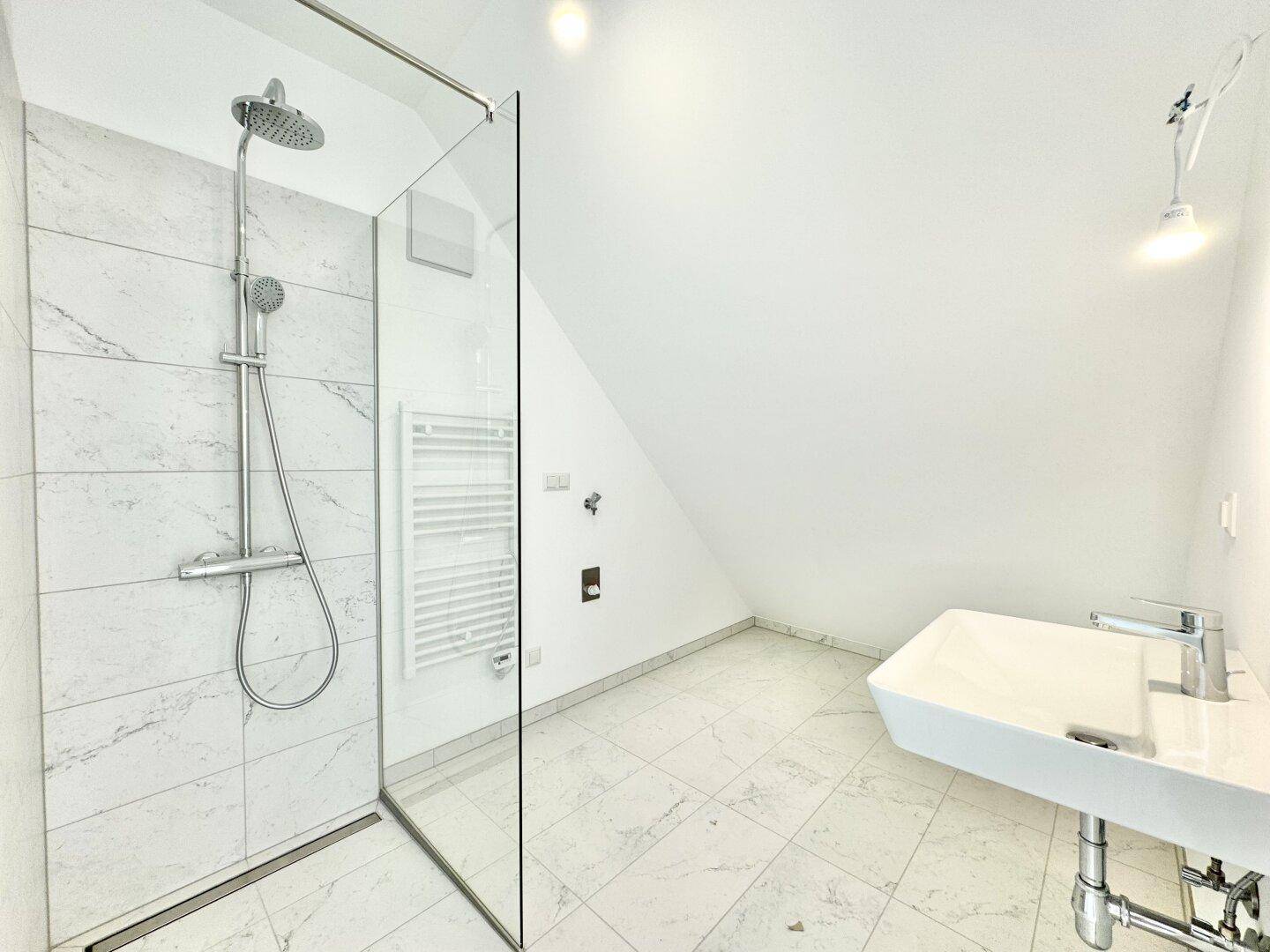 Modernes Badezimmer mit begehbarer Dusche, Marmorfliesen und Einzelwaschbecken unter schräger Decke.