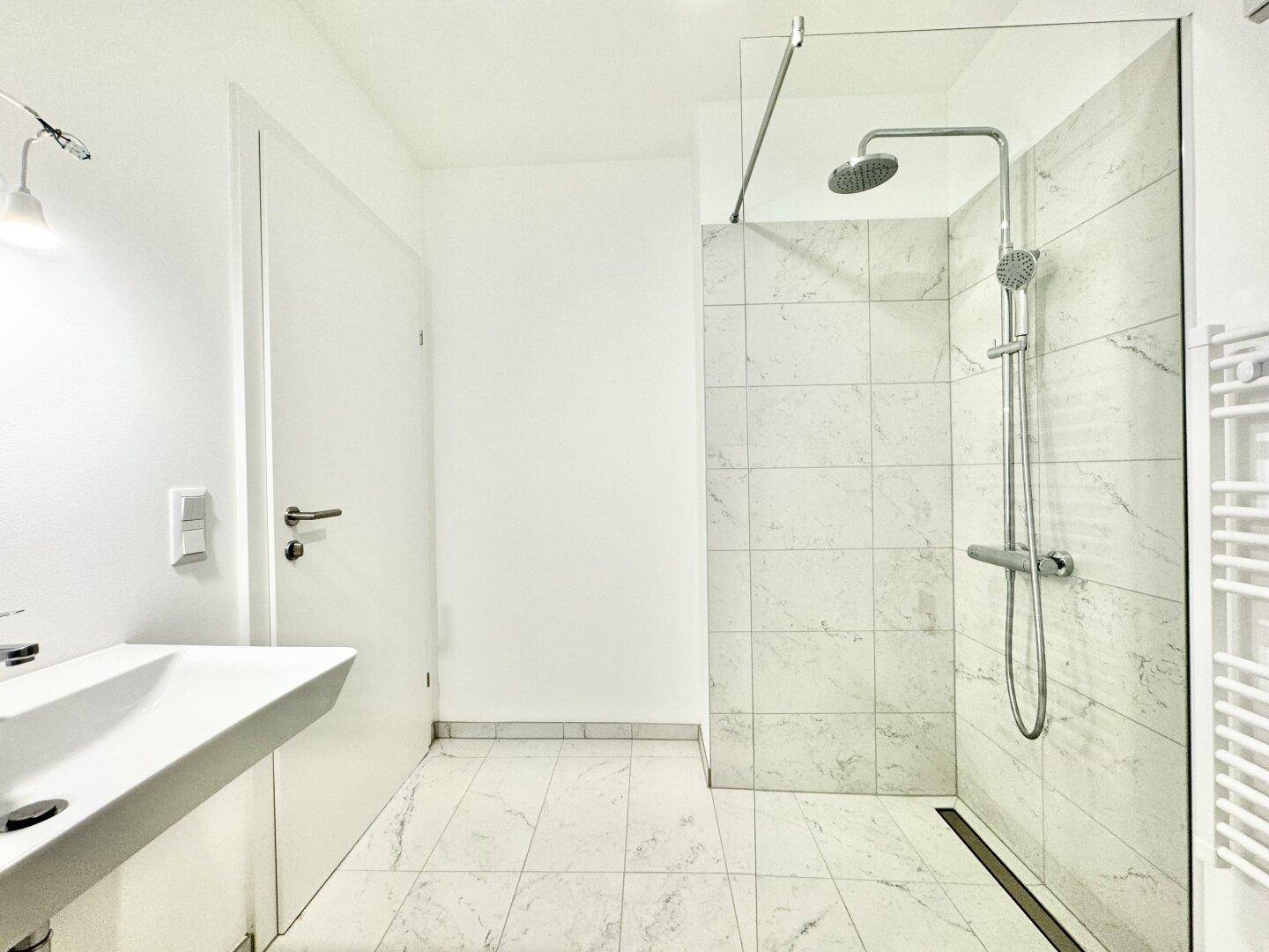 Helles Badezimmer mit begehbarer Dusche, Marmorfliesen, Einzelwaschbecken und Handtuchheizkörper.