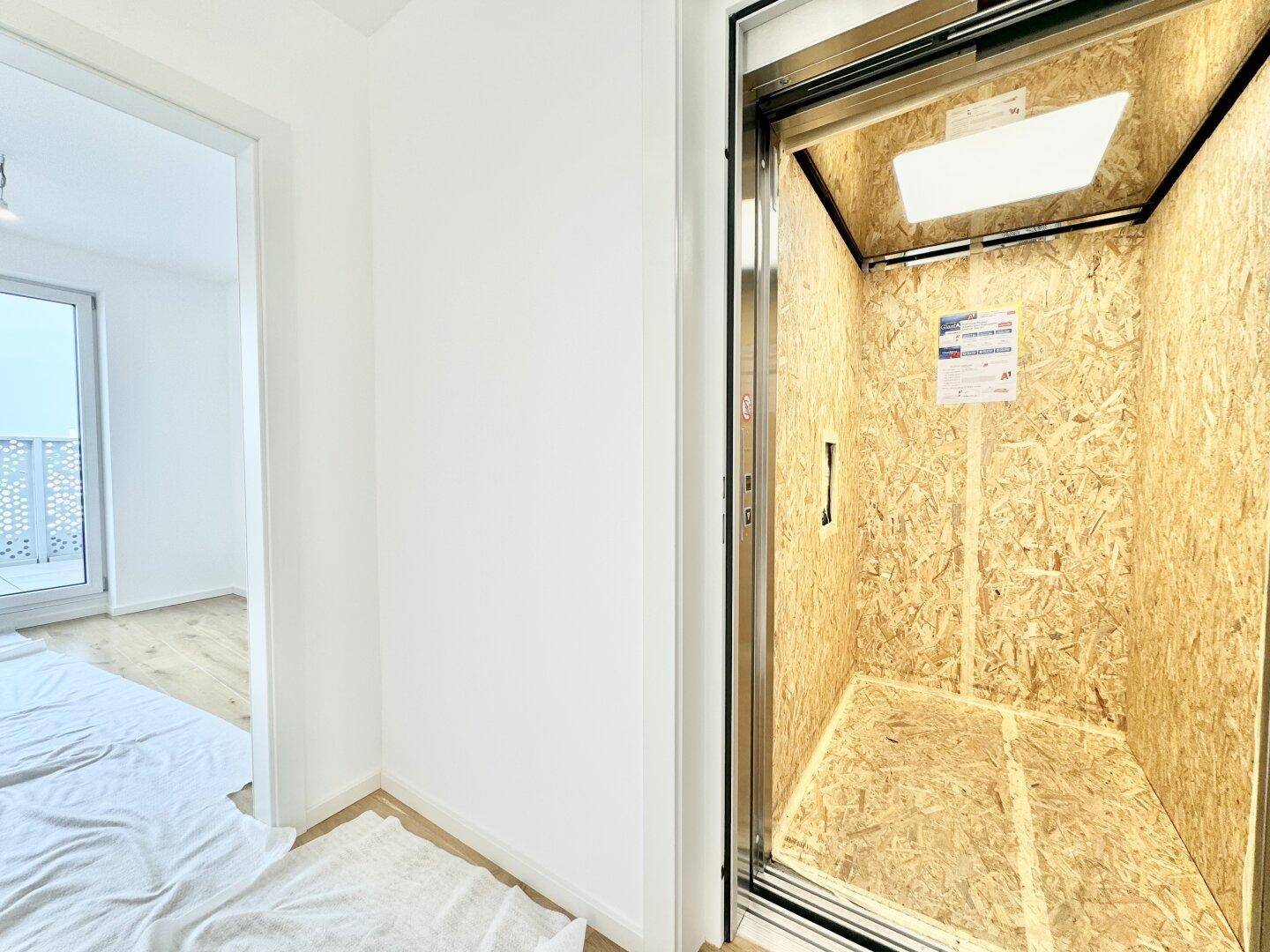 Innenansicht einer Aufzugskabine, derzeit mit Holzplatten zum Schutz verkleidet.