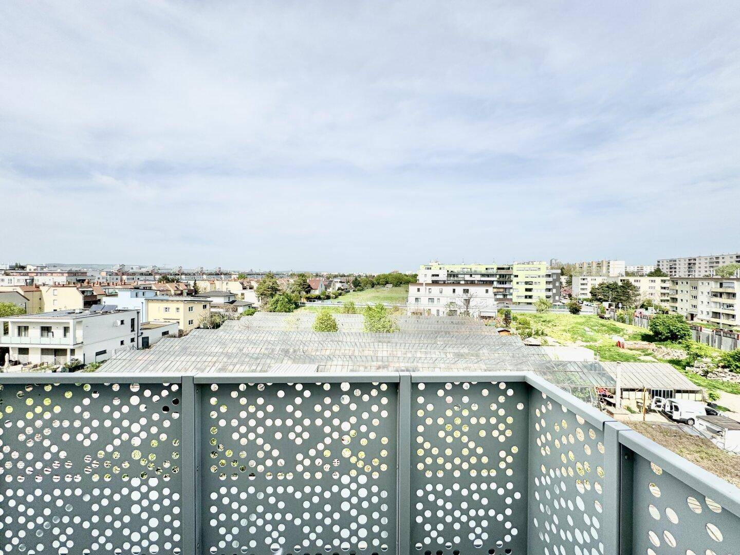 Weitblick von einem Balkon über die Stadt mit grünen Flächen und umliegenden Gebäuden.