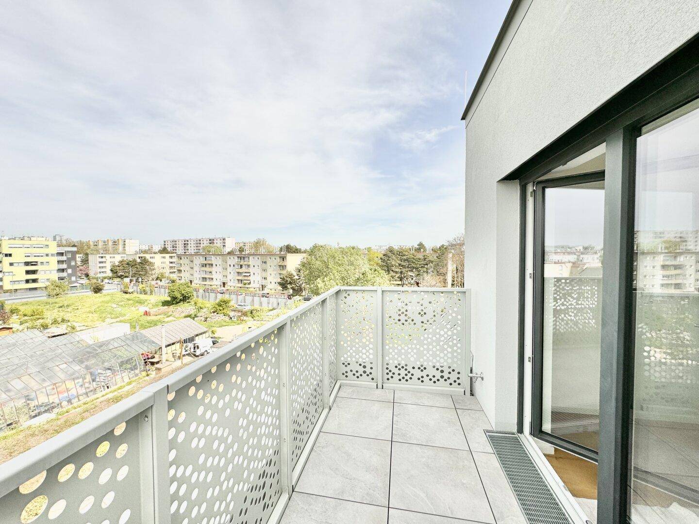 Balkon mit Fliesenboden und moderner Brüstung, bietet Blick auf Grünflächen und Gebäude.